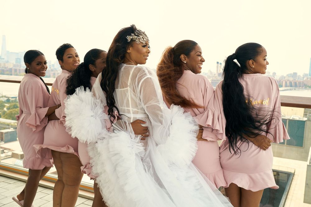 Wedding party in pink robes poses together on a balcony with cityscape views. at the WIlliam Vale Hotel