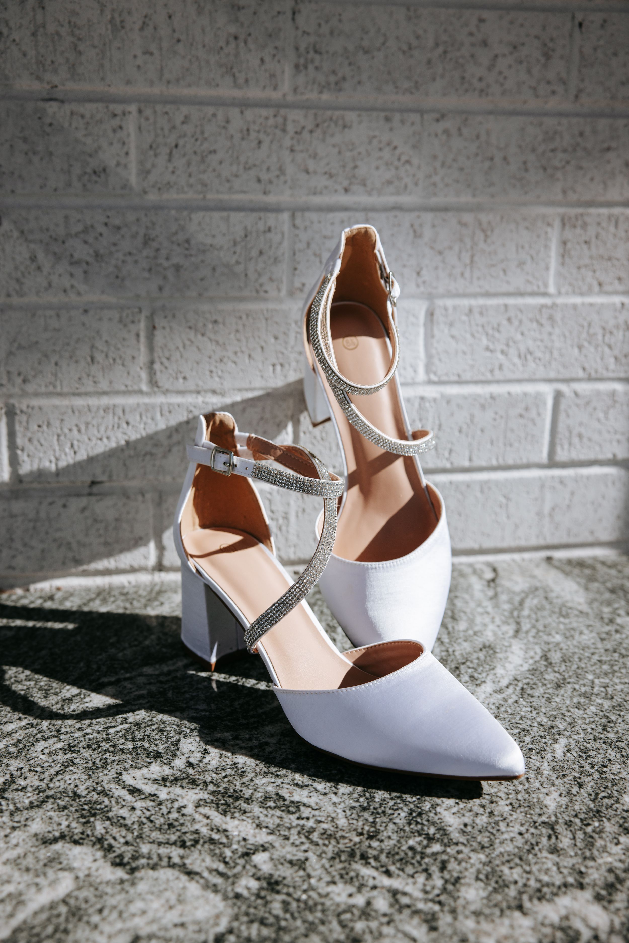 A series of elegant white bridal shoes displayed against a textured concrete background.
