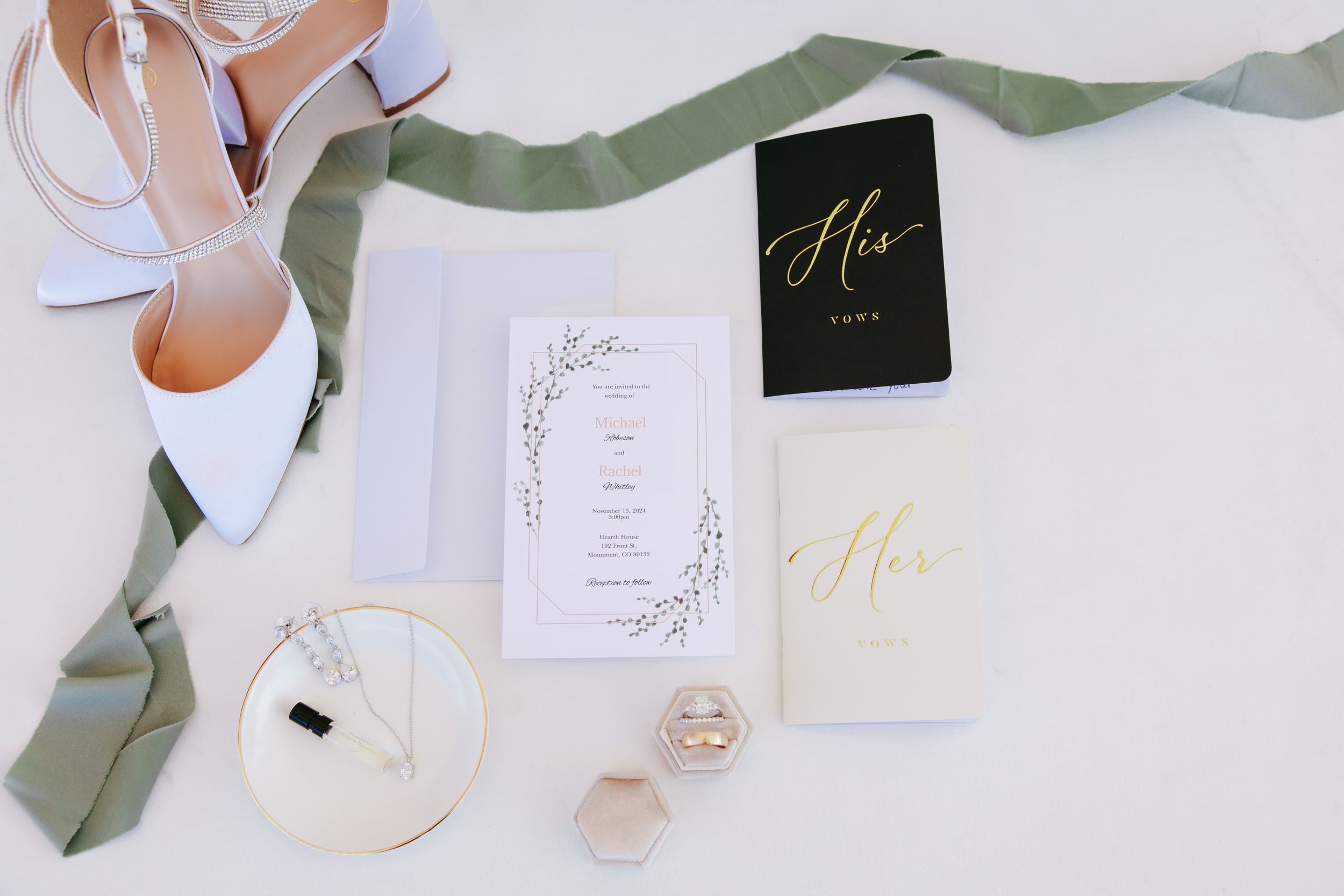 Wedding invitation suite with gold foil details, sage green ribbon, and modern black and white stationery.