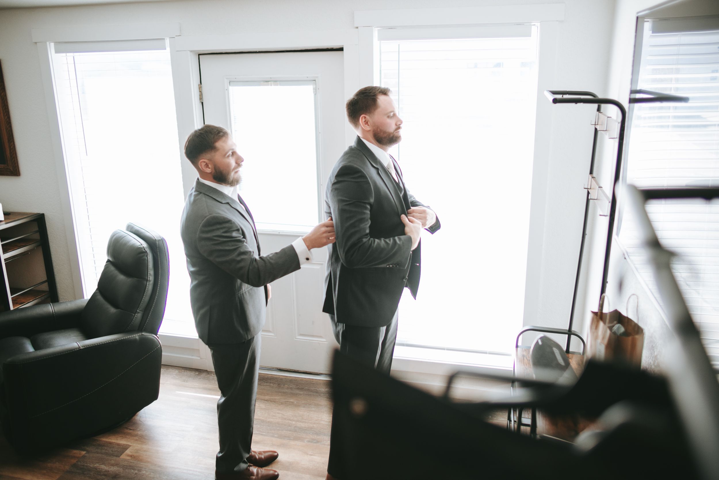 Two men in matching green suits standing in a room with white window.