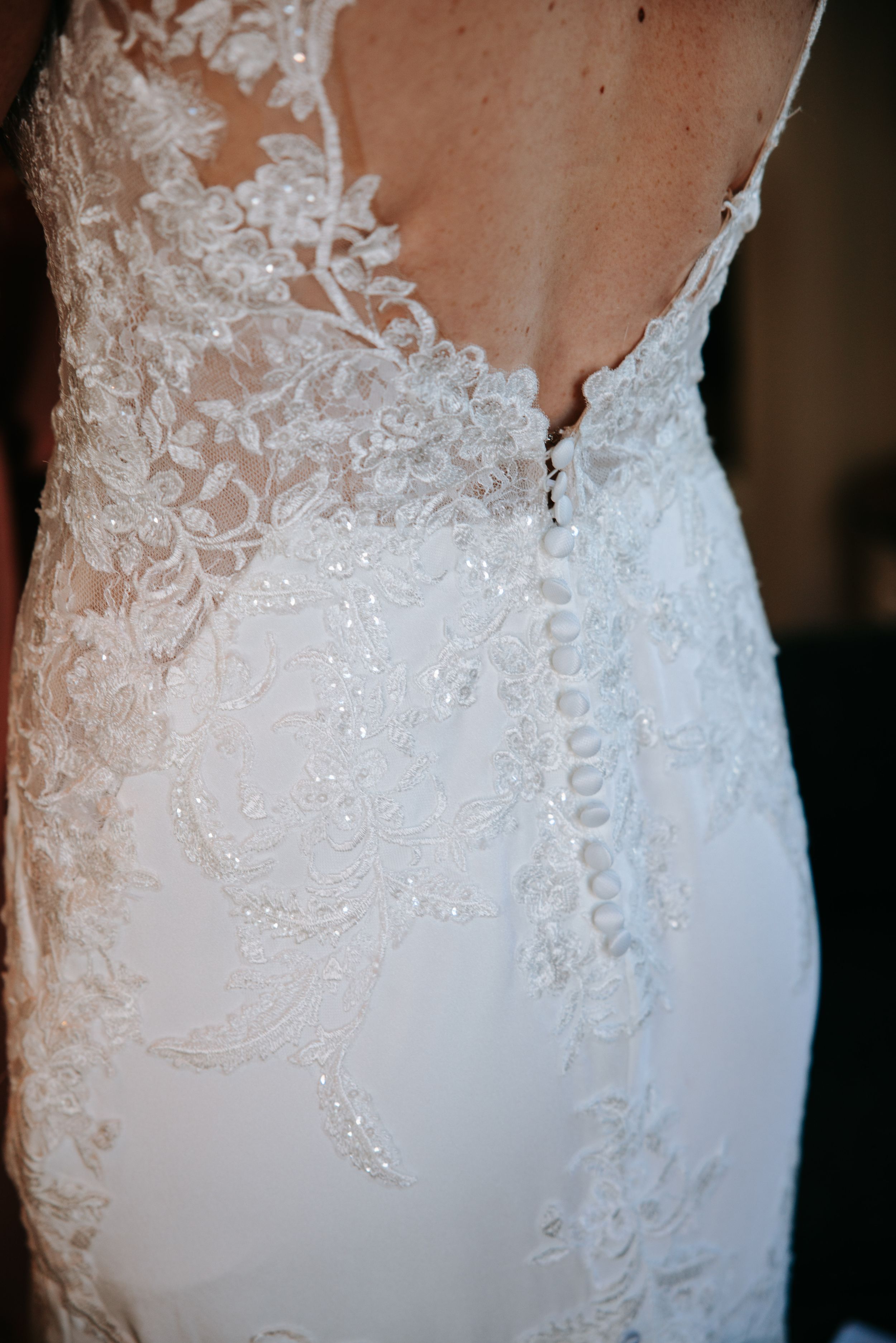 Close-up detail of an elegant white lace wedding dress bodice with intricate embroidered floral patterns.