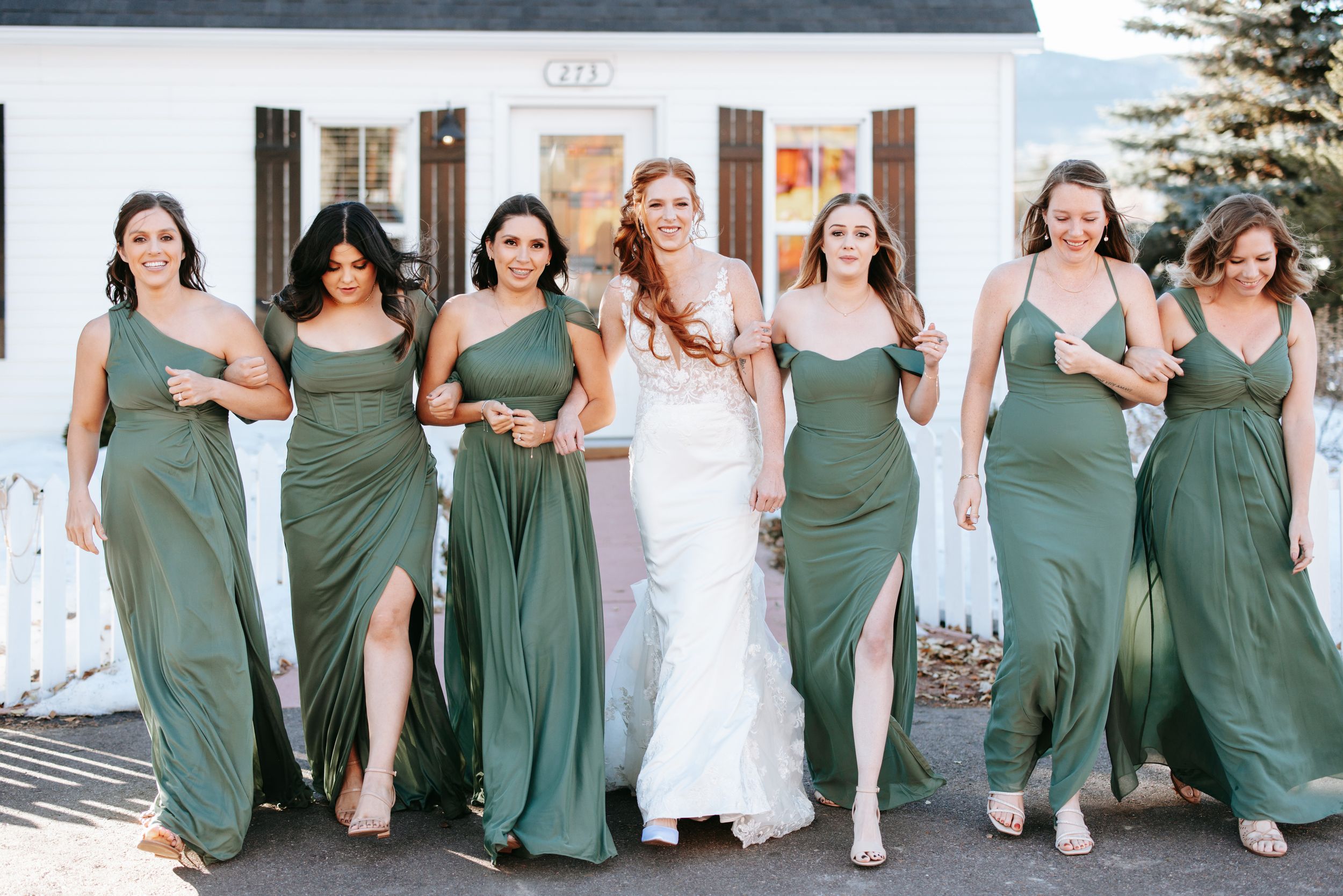 Bridesmaids wearing matching sage green dresses walk together and laugh during a wedding celebration.