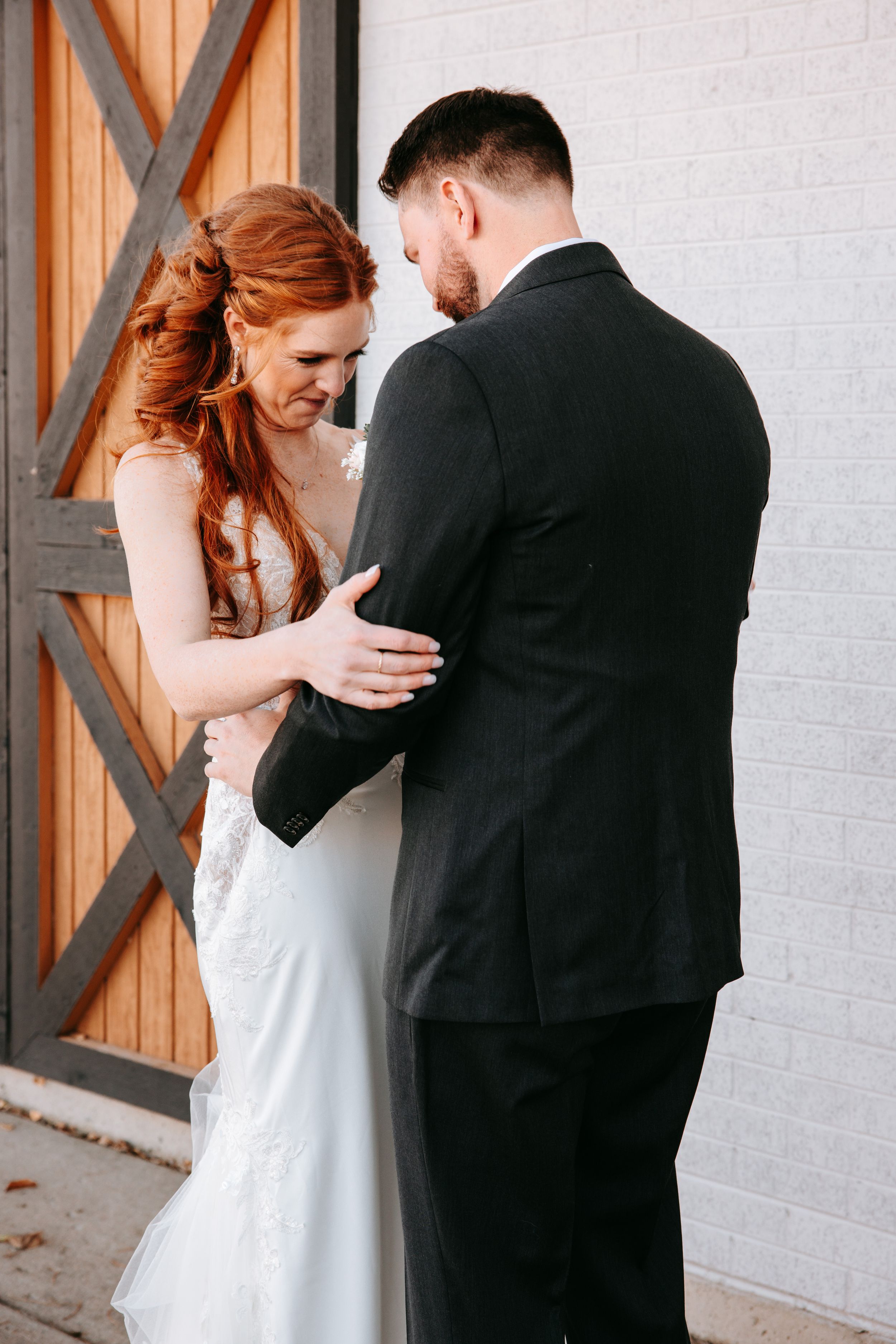 Elegant wedding couple sharing intimate moments against a white brick wall with wooden accents.