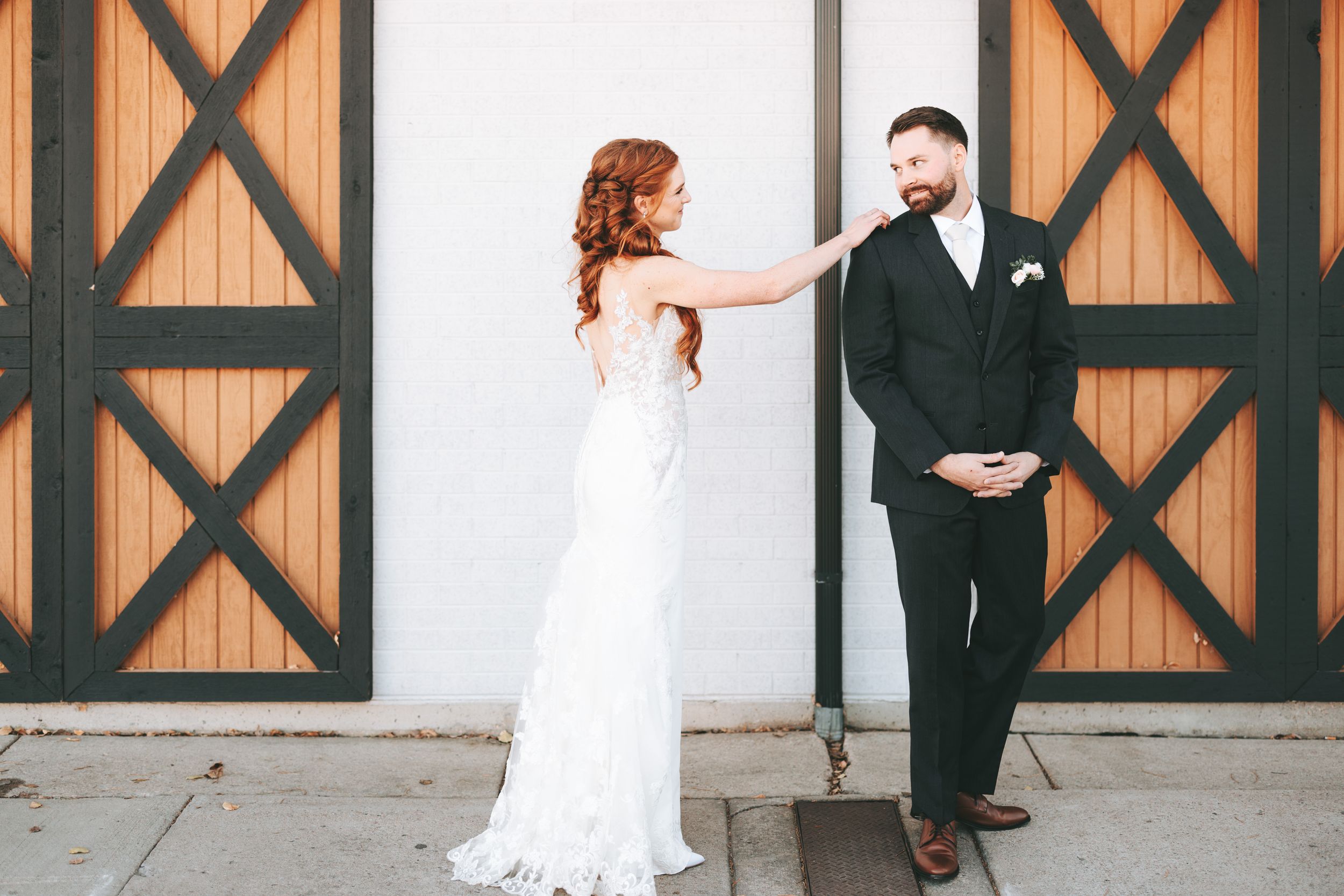 Wedding couple dances and poses in front of rustic black barn doors at venue.