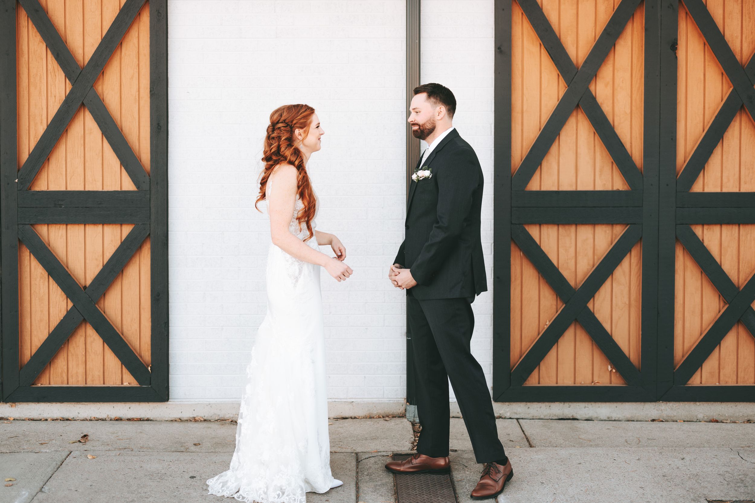 Elegant wedding couple standing in front of rustic wooden barn doors with geometric patterns.