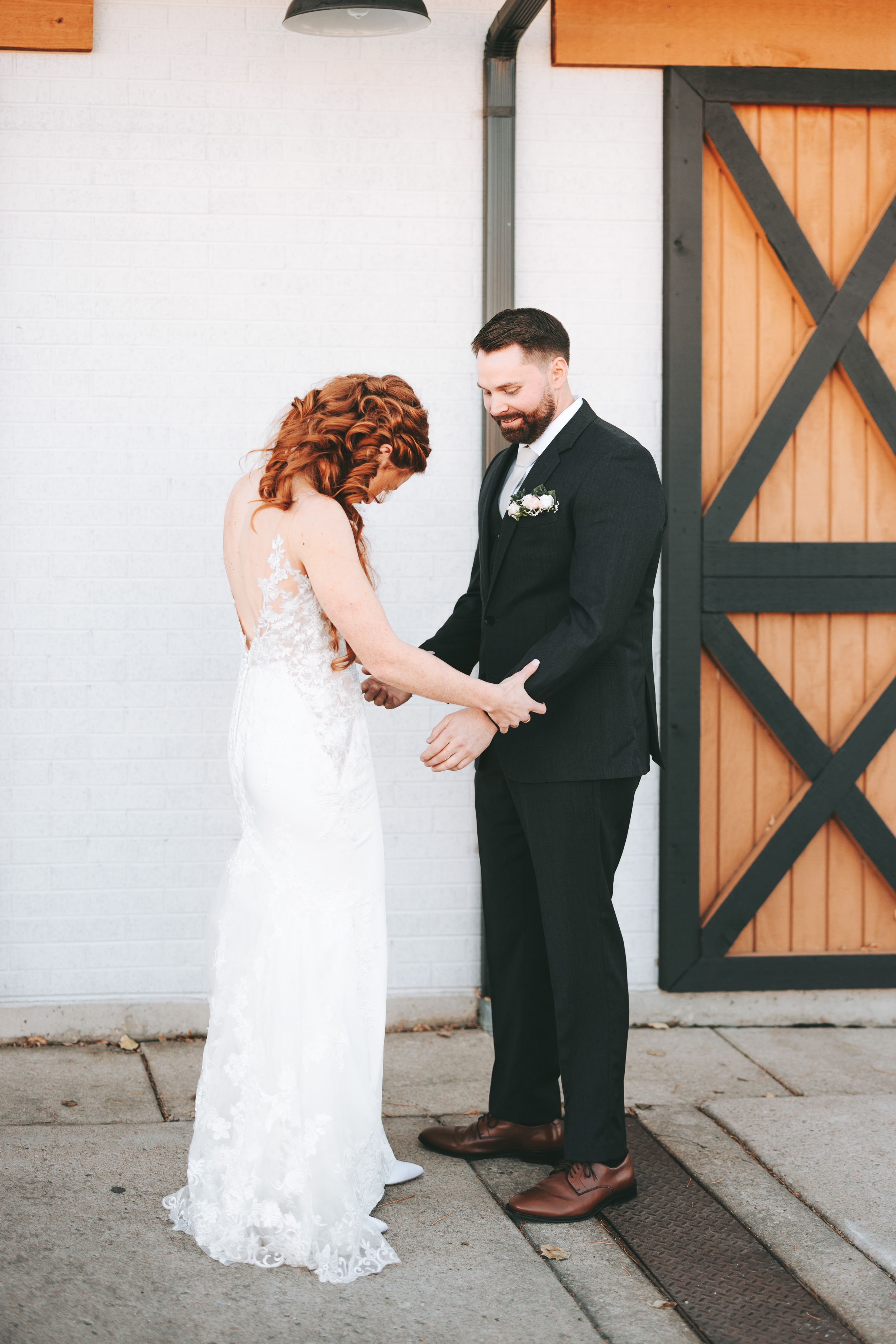 A couple shares an intimate first look moment before their wedding against a white wall with wooden barn doors.