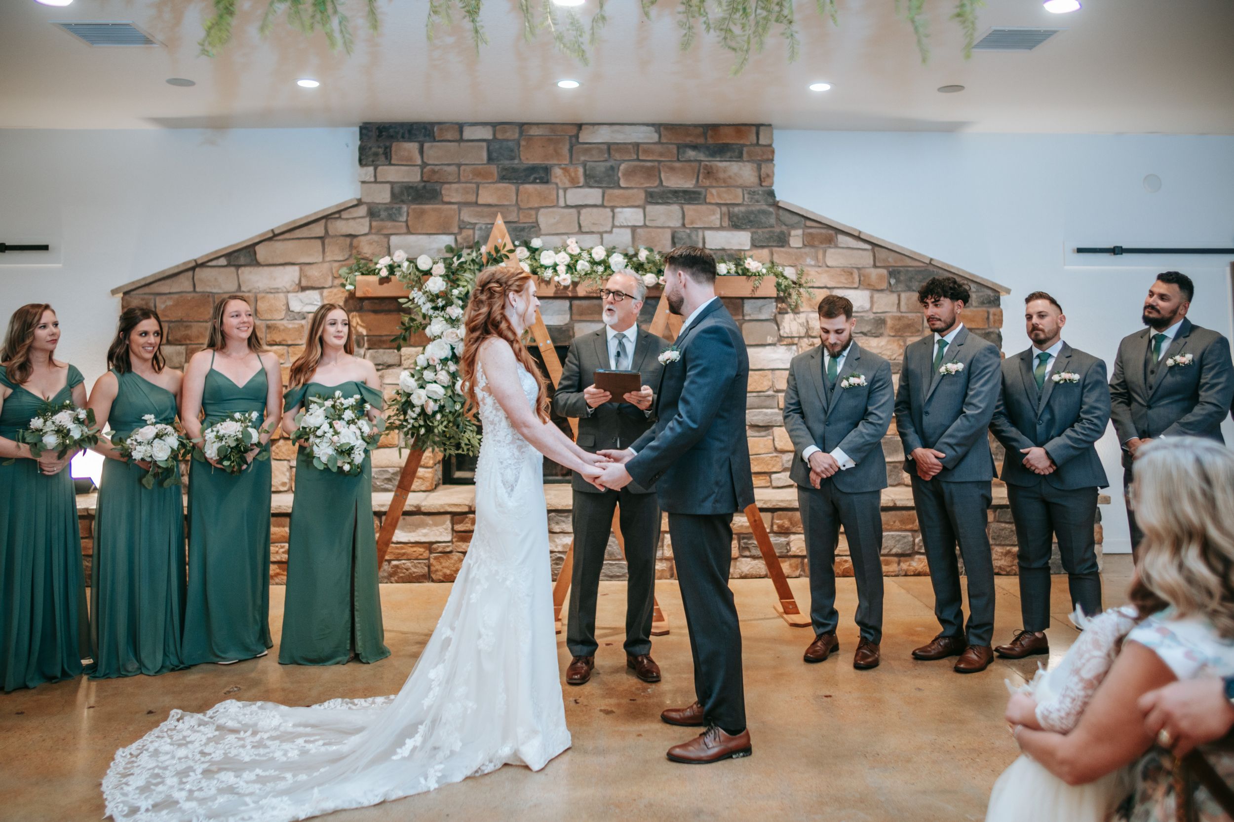 Wedding ceremony in a rustic indoor venue with exposed brick wall and hanging floral decorations.