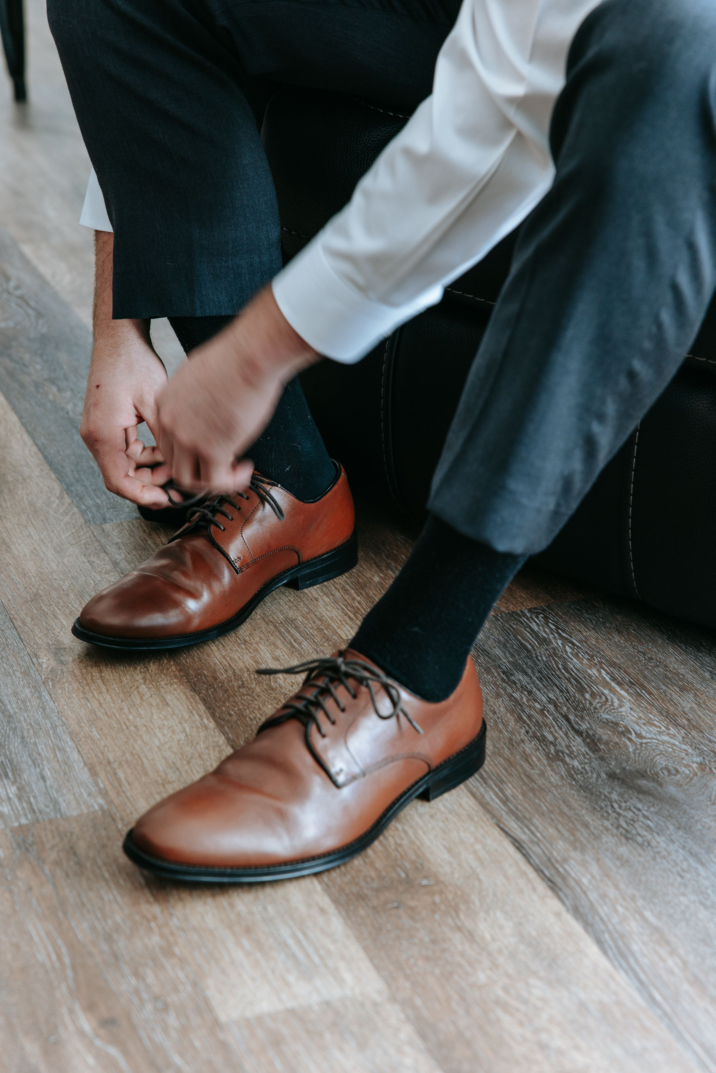 Close-up sequence of brown leather dress shoes being laced up on wooden flooring.