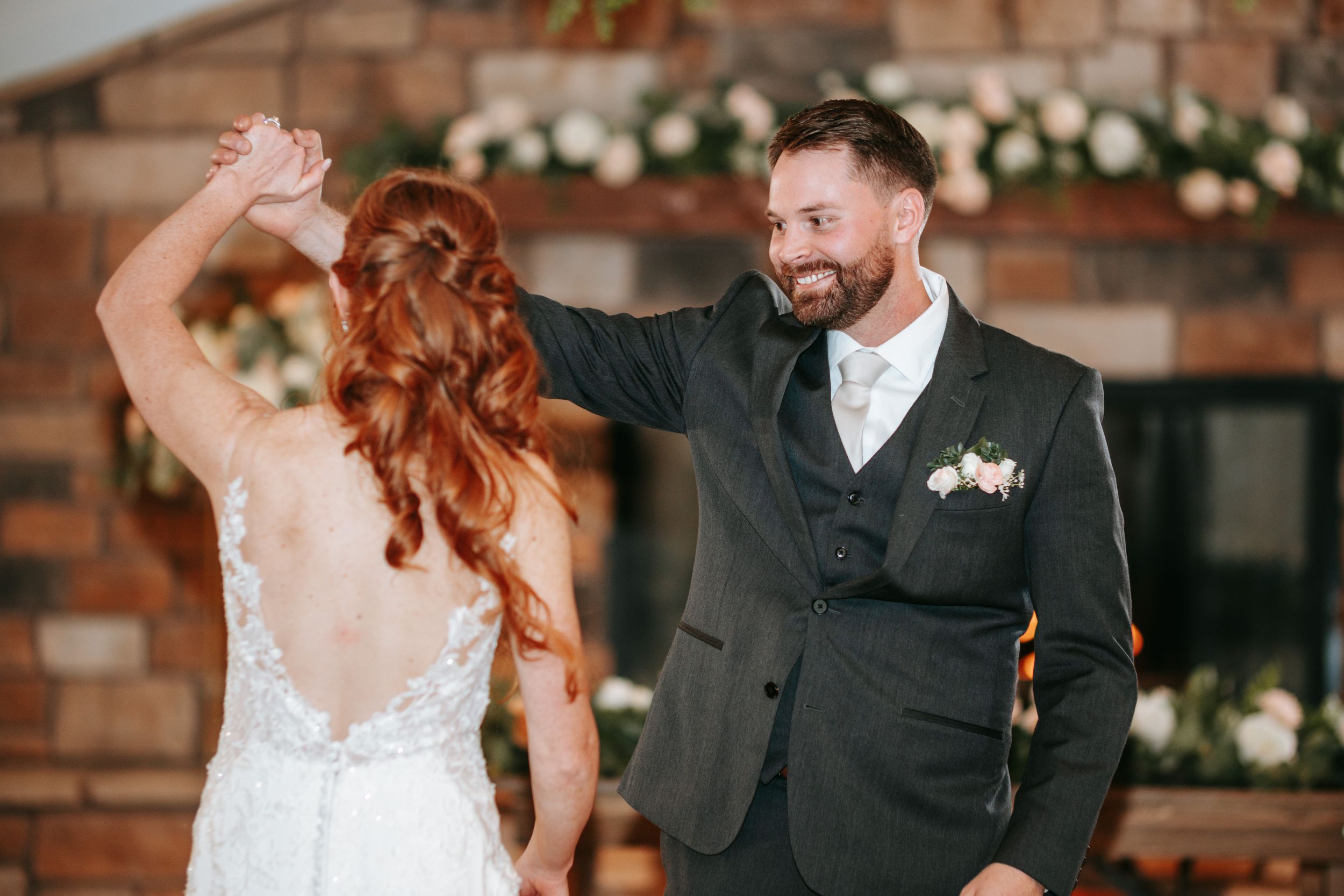 A joyful couple dancing together at their wedding celebration with brick walls and floral decorations in the background.