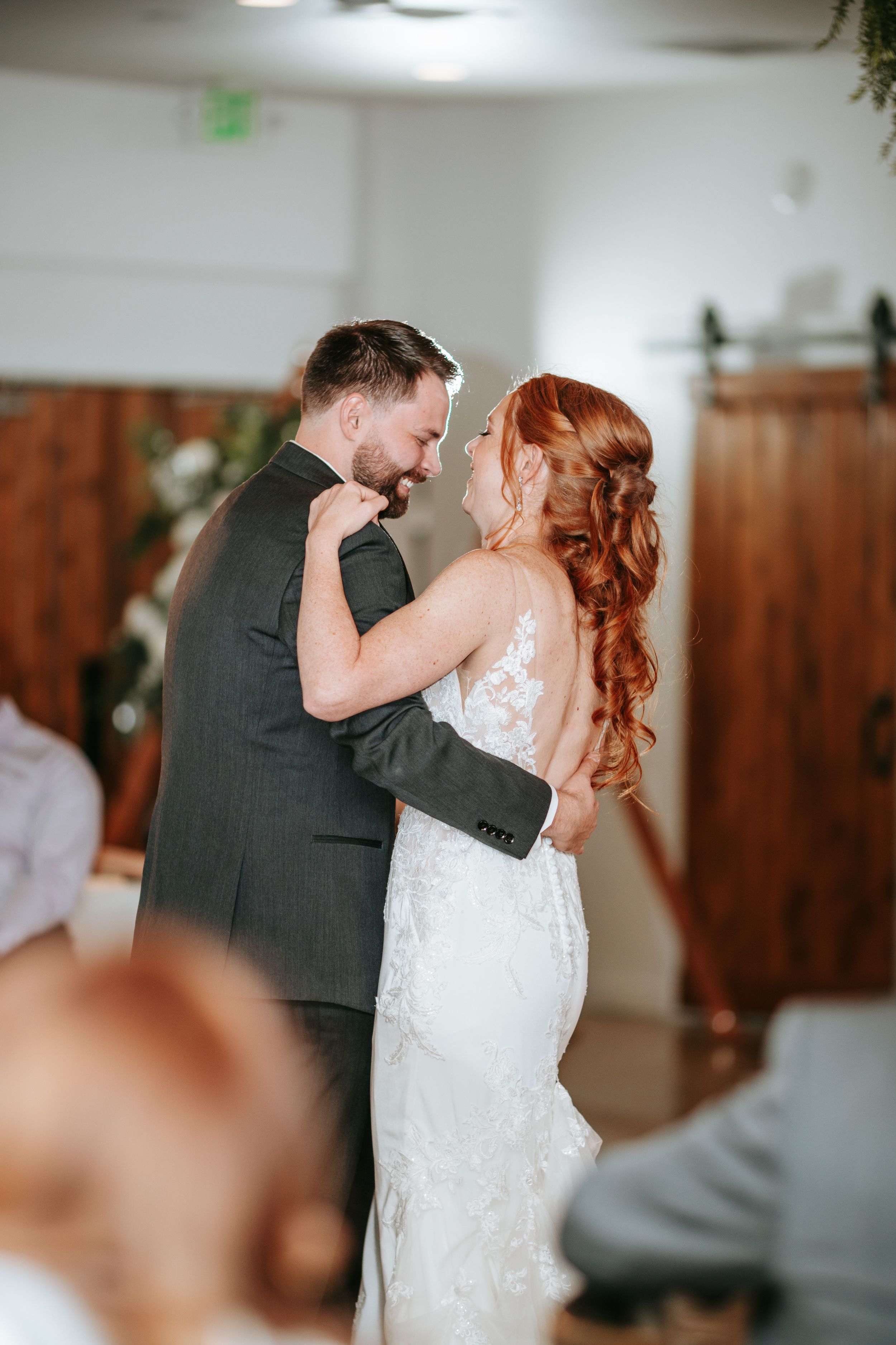 A bride and groom share their first dance together at their wedding reception with wooden wall decor in the background.