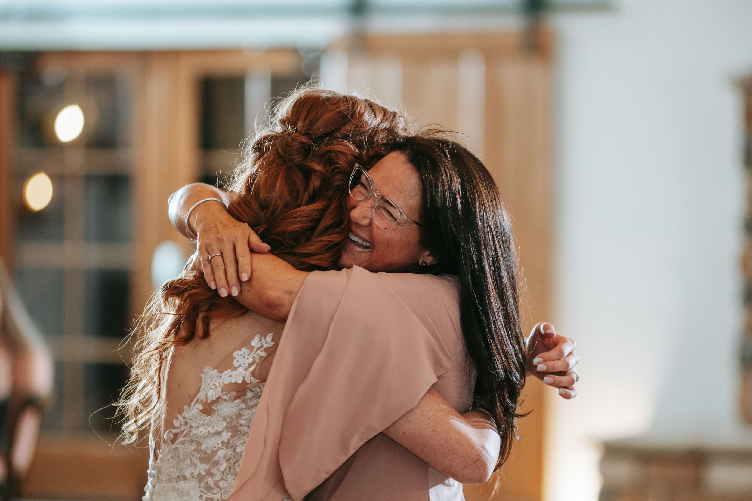 Guests share emotional embraces during a wedding celebration in a warmly lit indoor venue.