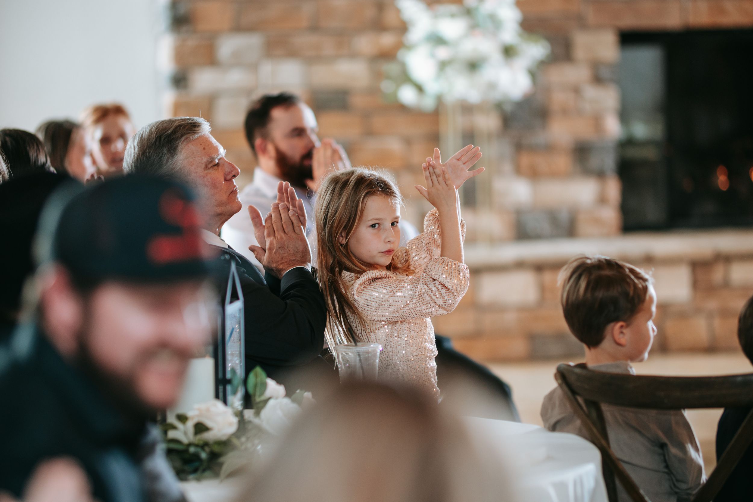 Wedding guests raise their hands in celebration at a rustic brick-walled venue during a festive reception.