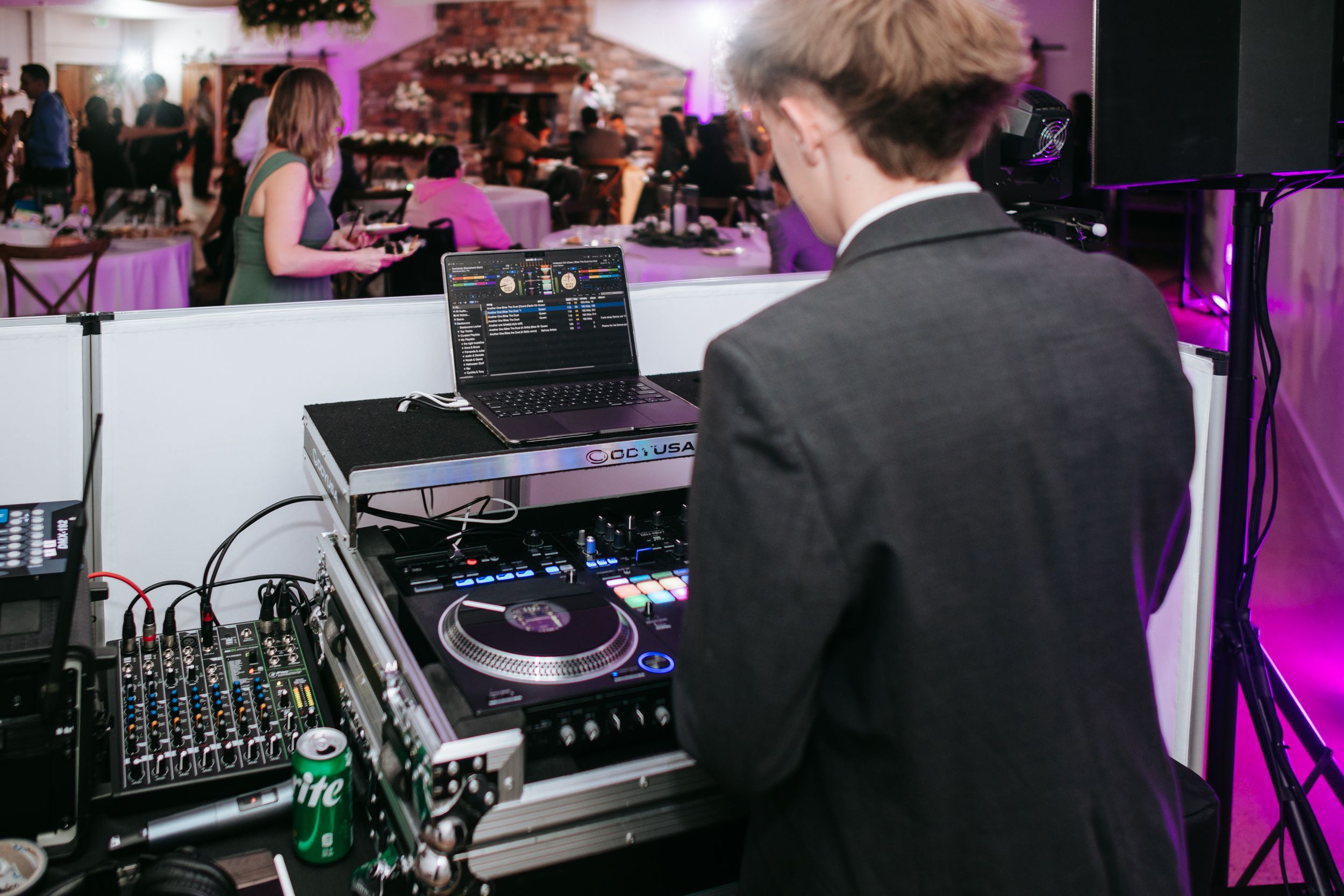 DJ equipment and controllers set up at an event with purple ambient lighting in the background.