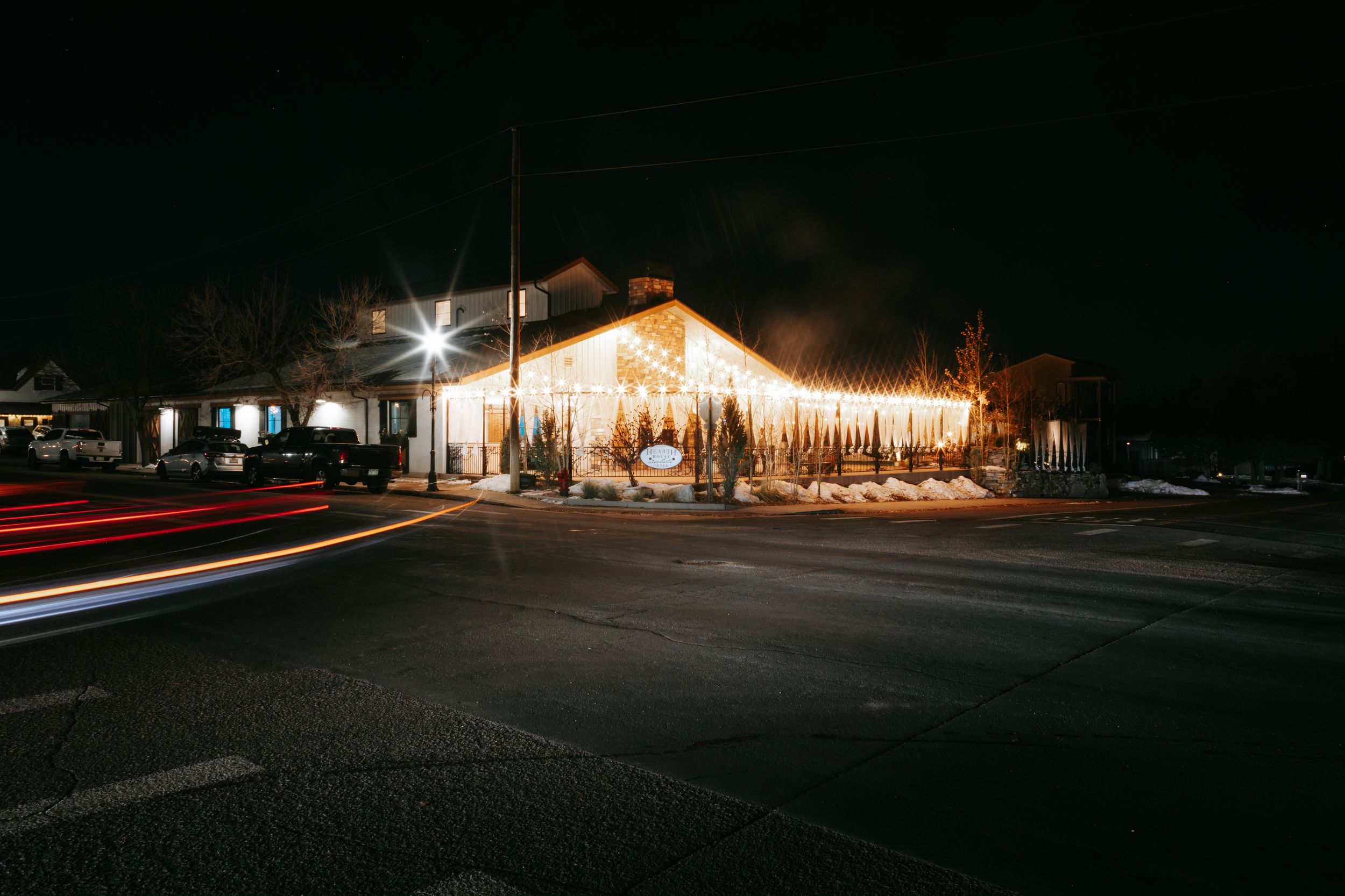 Warmly lit wedding venue exterior glowing at night with light trails from passing cars in the parking lot.