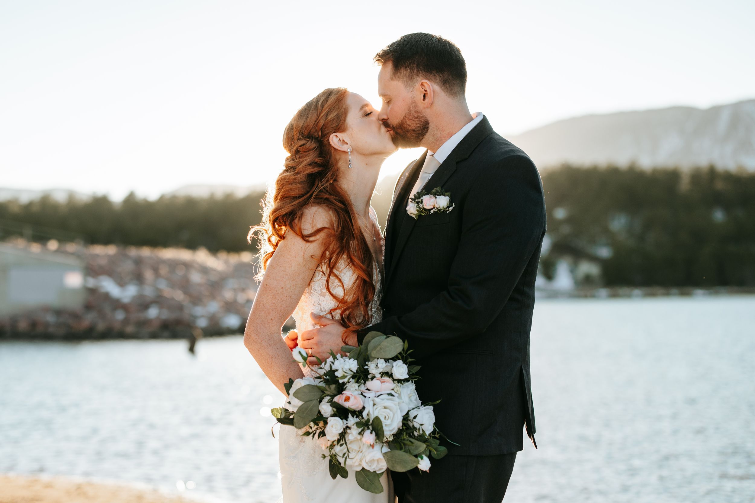 A romantic seaside wedding portrait with mountains in the background and white floral bouquet.