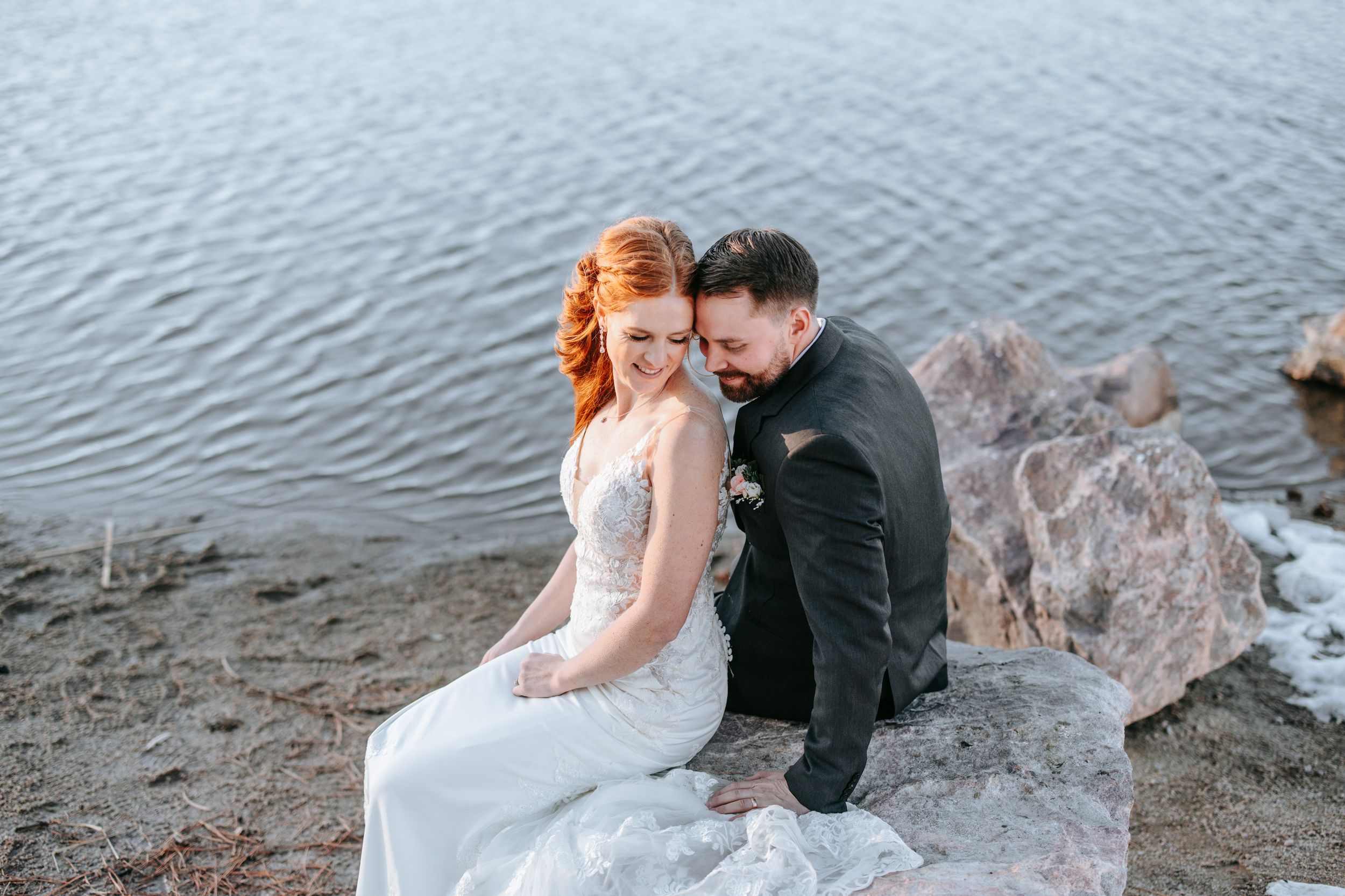 Romantic couple in wedding attire sitting together by a serene lake.