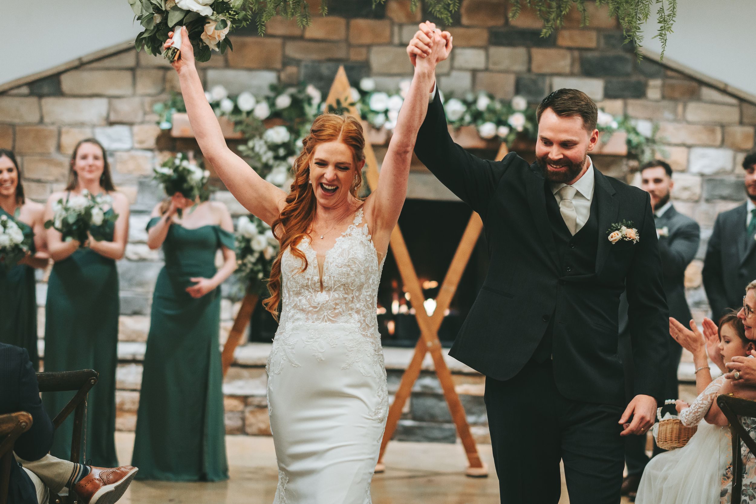 A couple celebrates at the end of their wedding ceremony while guests look on in a rustic stone venue.