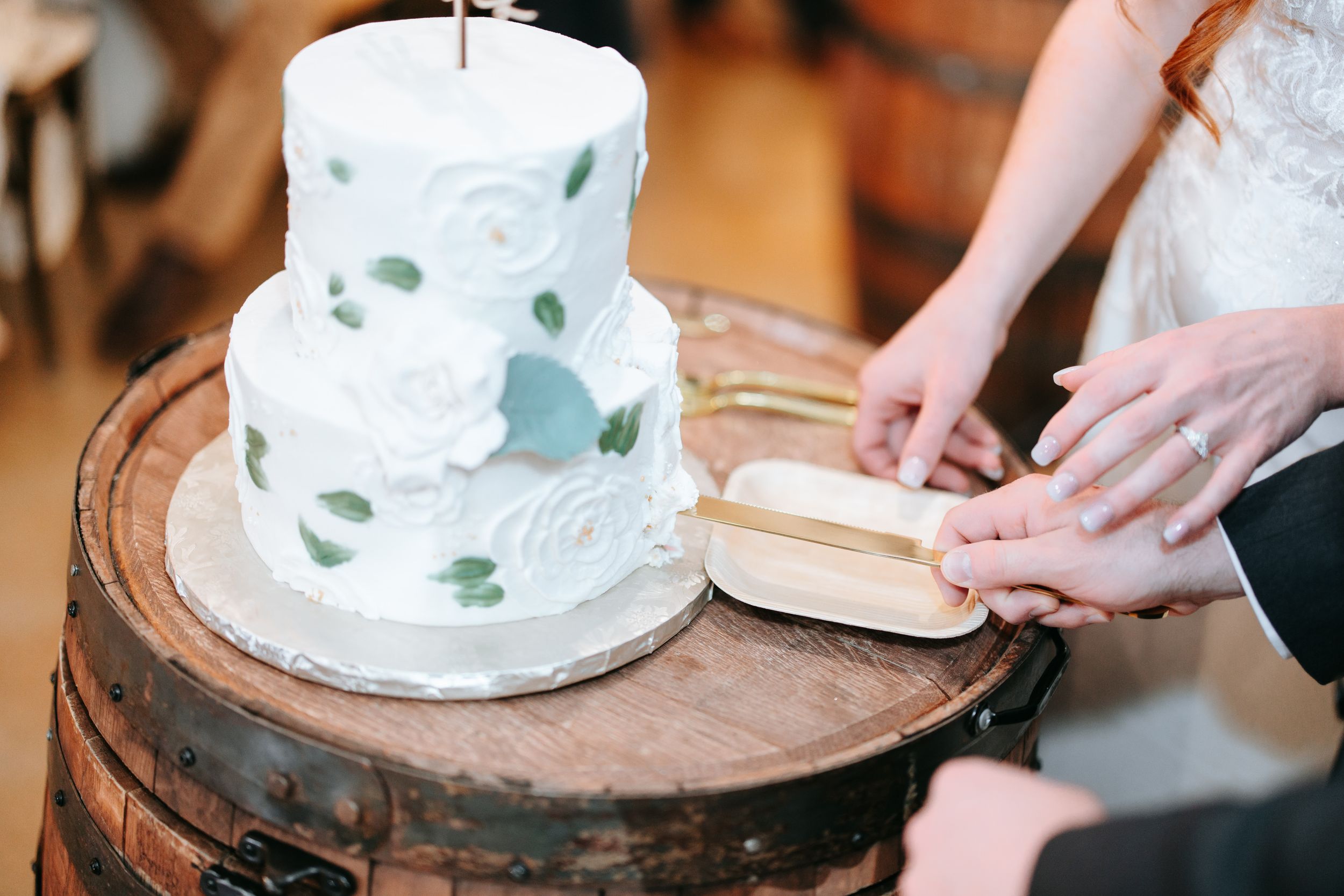 Newlyweds cut their simple white wedding cake together on a wooden cake stand during the reception.