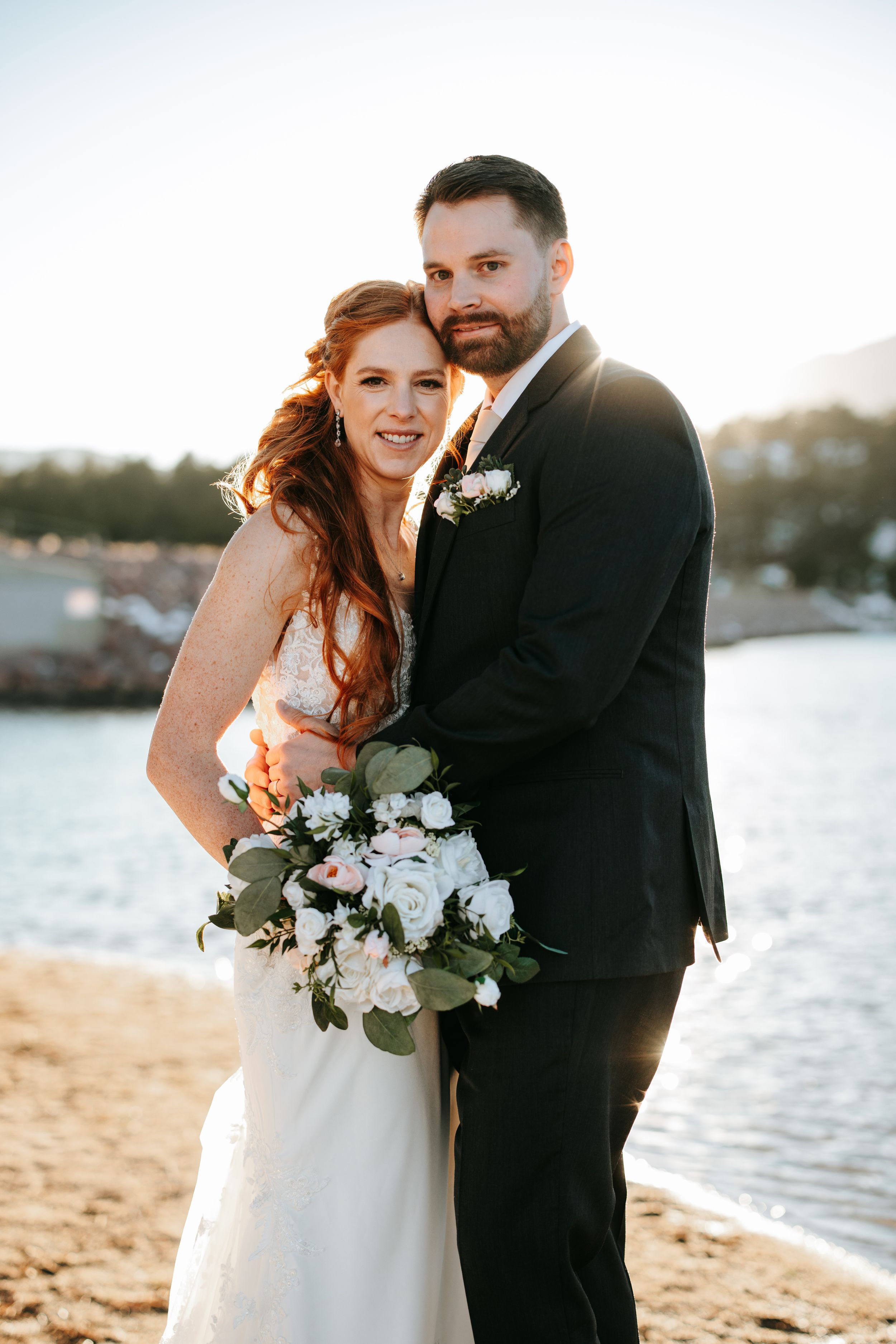 A beachside wedding portrait with elegant white floral bouquet and waterfront scenery at sunset.