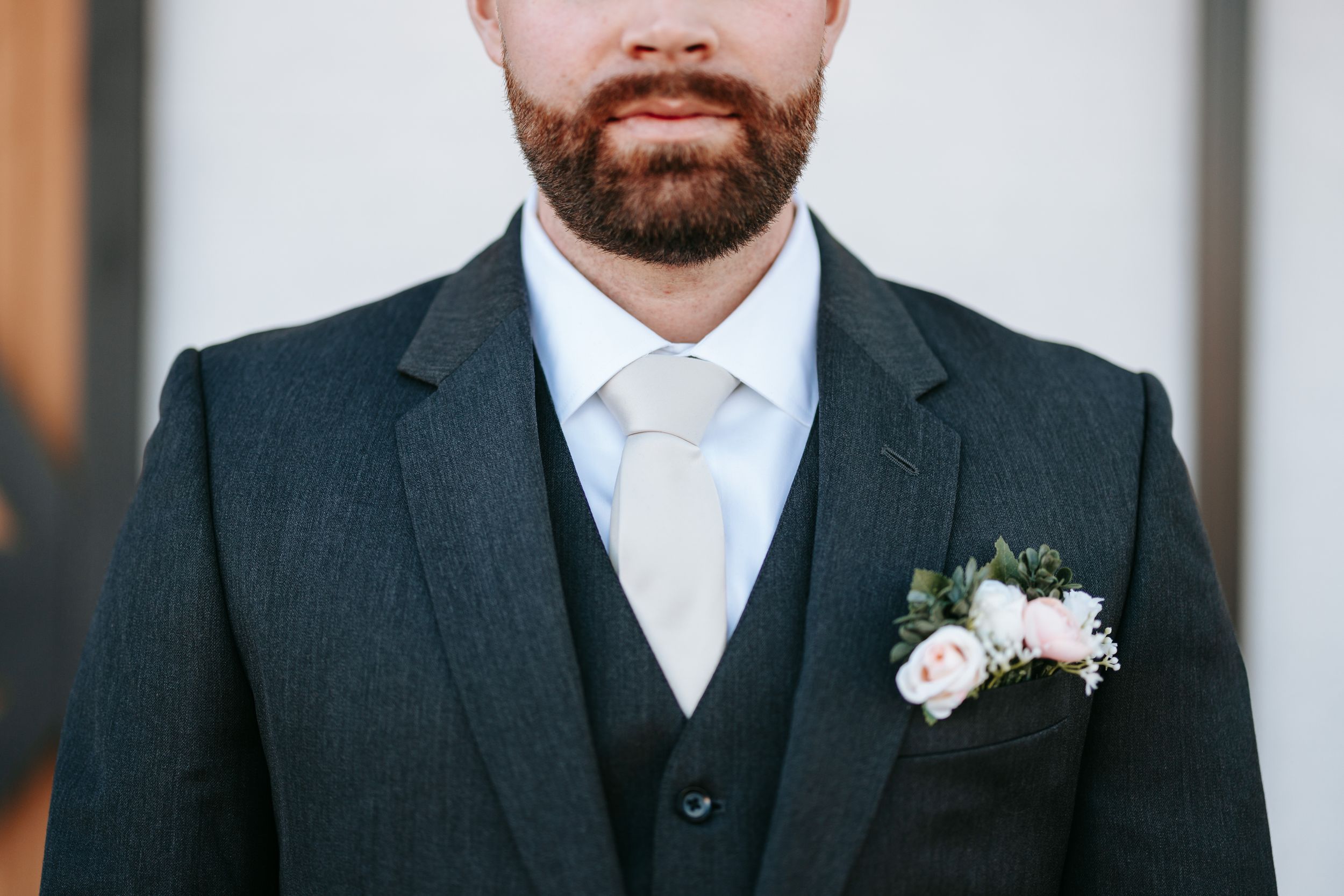 Close up detail of a groom wearing a dark suit with white tie and floral boutonniere.