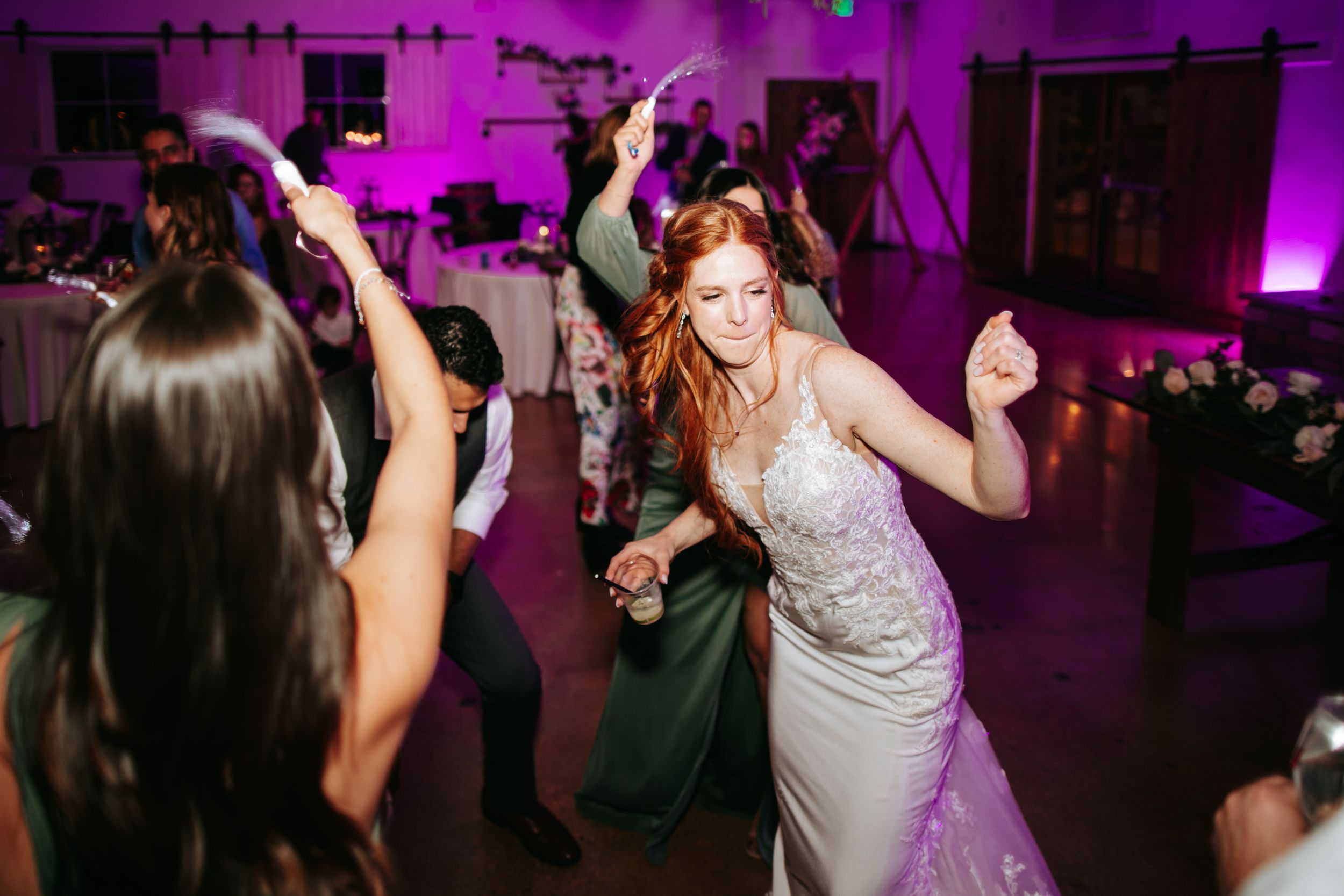 Dance floor filled with celebration under purple mood lighting at an evening event.