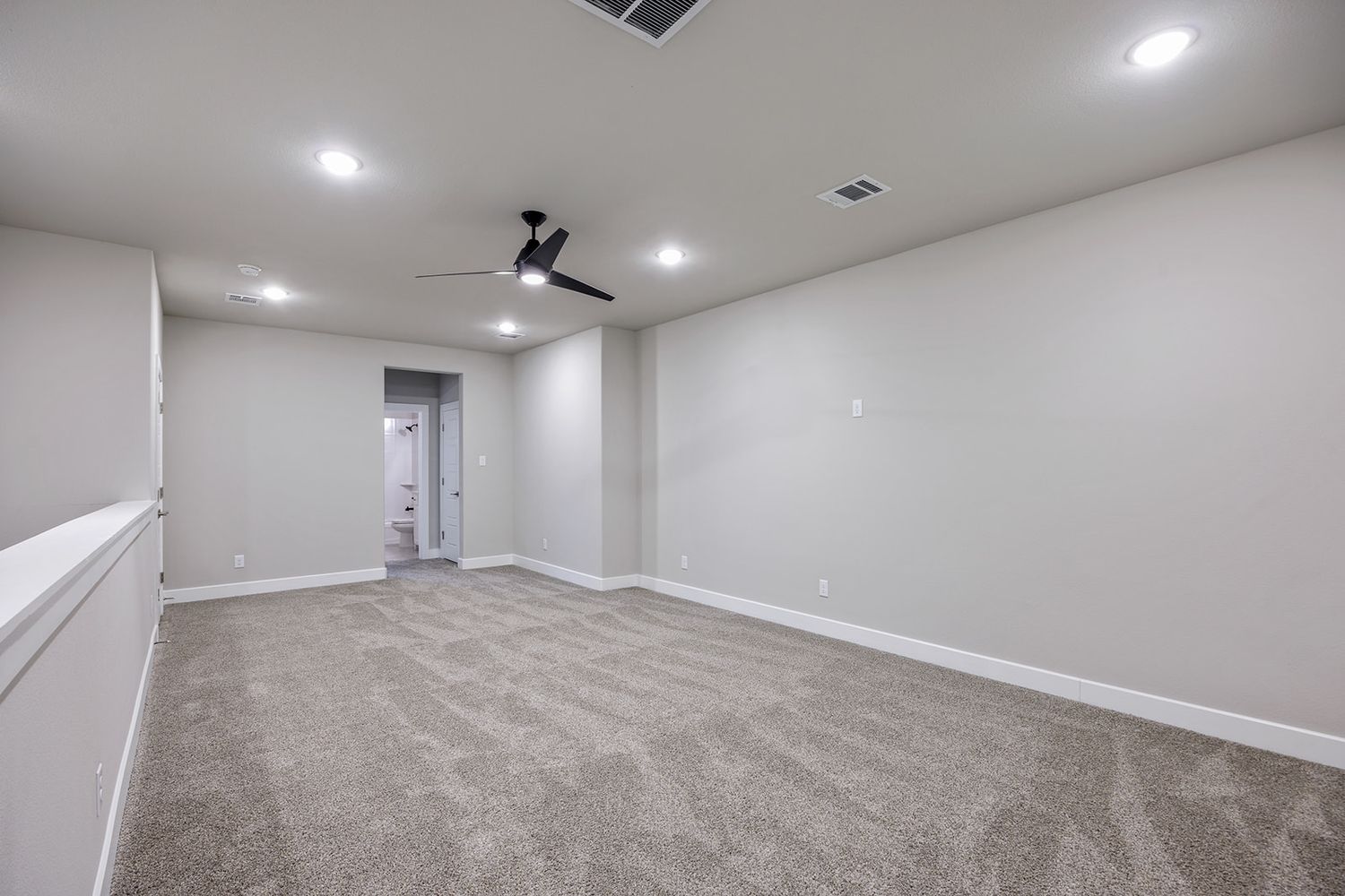 Empty room with gray carpet, white walls, recessed lighting and ceiling fan in modern residential interior.