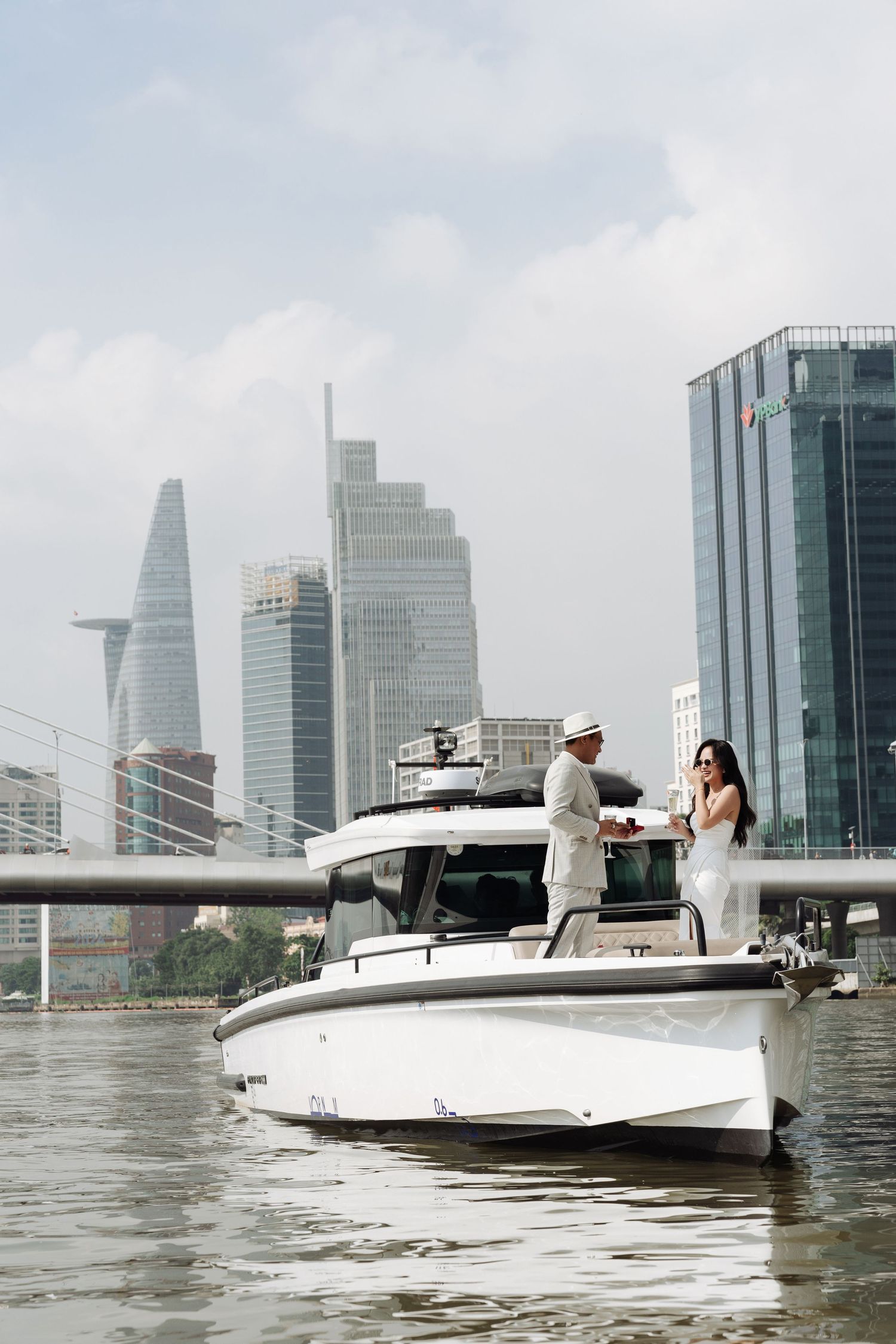 Couple standing on luxury white yacht with Ho Chi Minh City skyline in background.