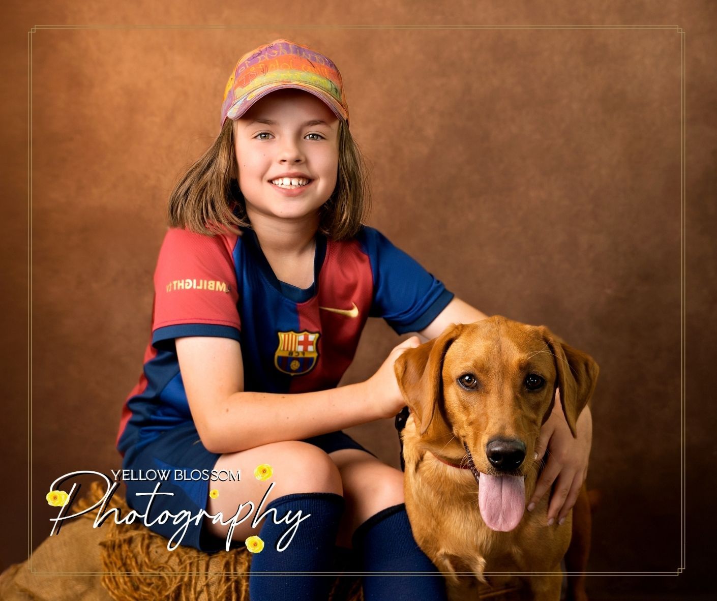 A brown dog with a floppy tongue poses for a portrait with someone wearing a Barcelona soccer jersey and baseball cap.