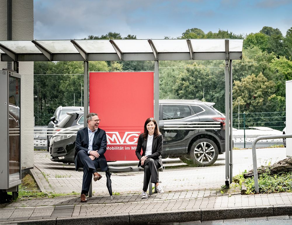 Geschäftsführer einer Verkehrsgesellschaft sitzen zusammen an einer Haltestelle, authentische Businessfotografie für Unternehmen.