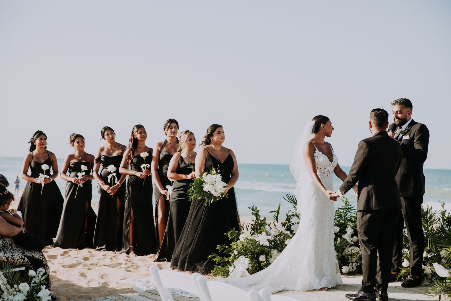 Wedding party and guests lined up on beach during sunset ceremony with ocean views.