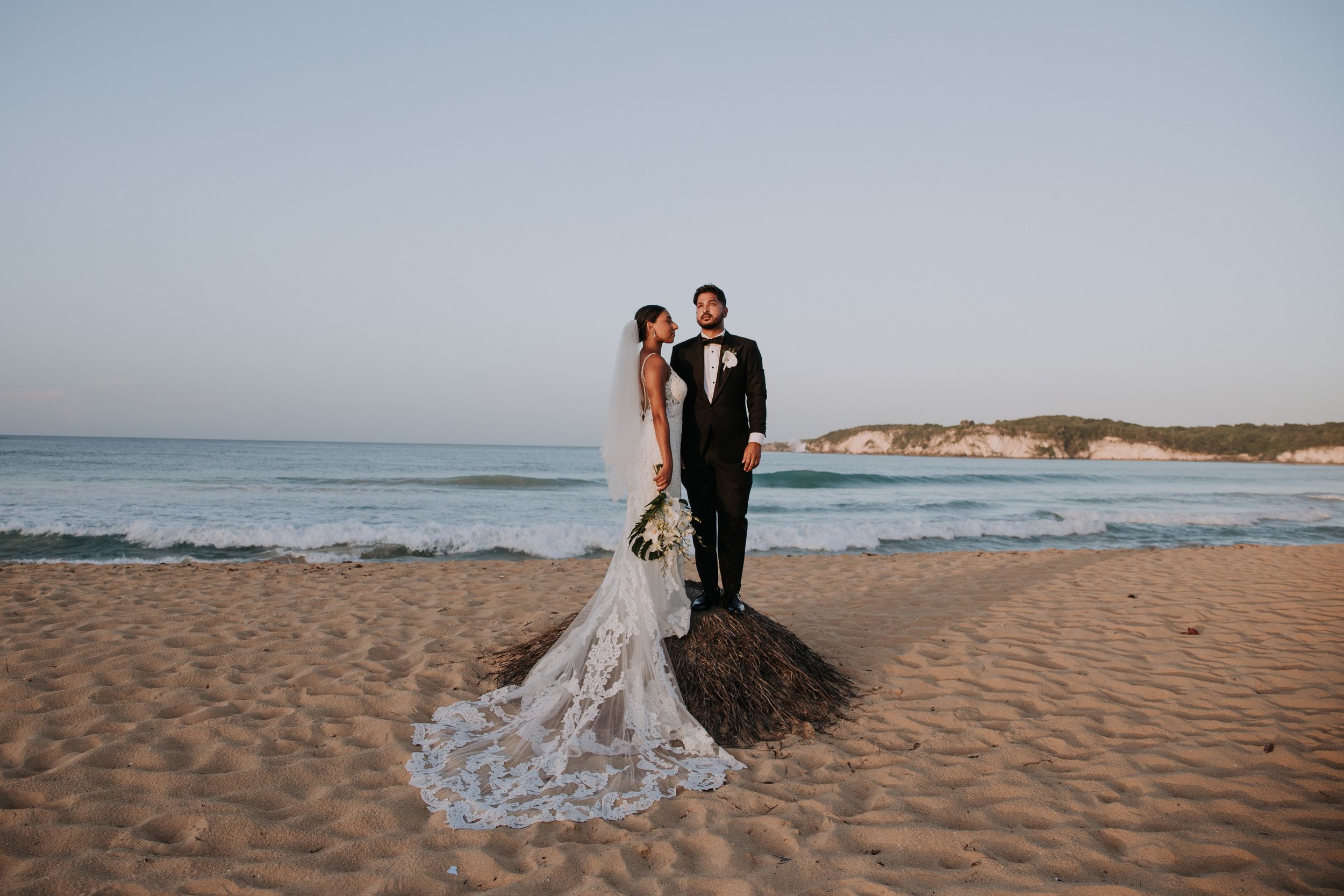 Beachside wedding photography capturing elegant couple and flowing lace dress train on sandy shore.