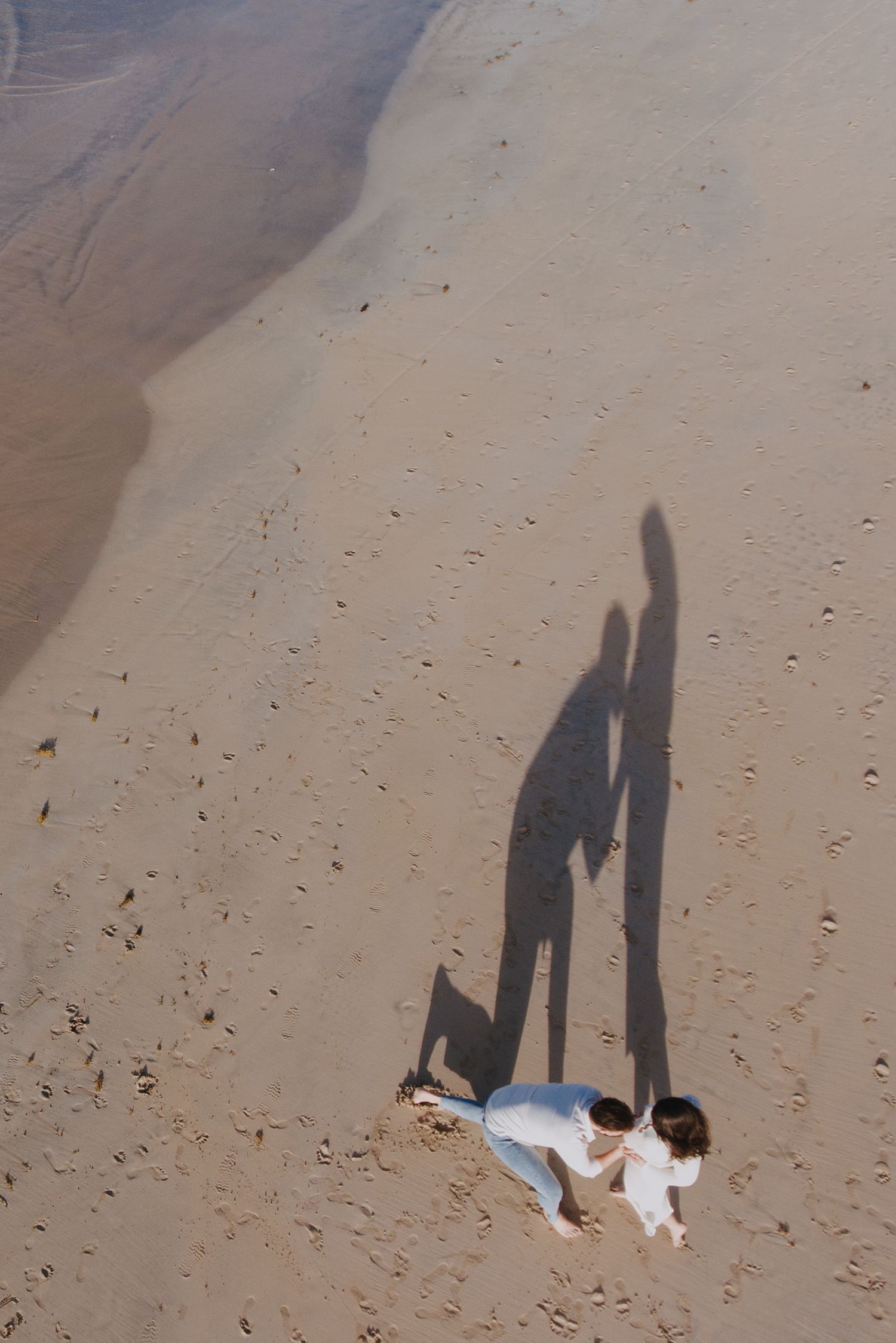 Aerial view of a couple on the beach creating long shadows in the sand.