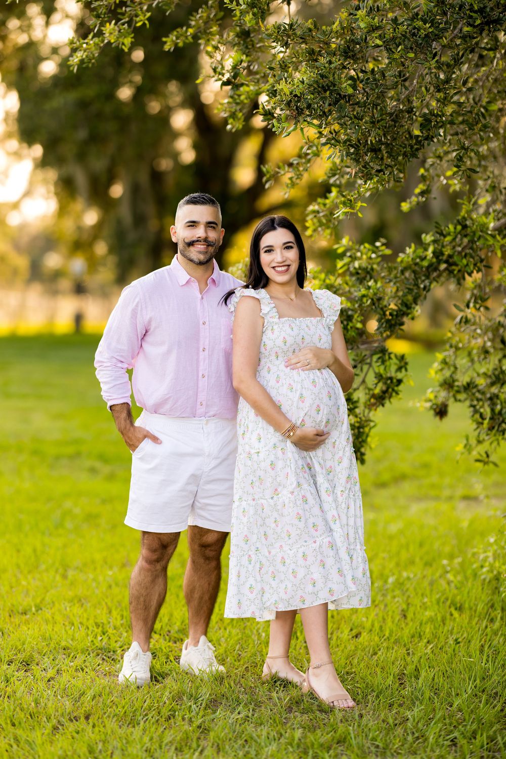Family poses together on grassy hill wearing coordinated white and pink outfits. Photo by Dani De La Rosa, DigitalMyst Photography, Florida