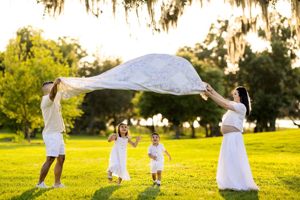 Family enjoying picnic and playtime on blanket in sunlit grassy field. Photo by Dani De La Rosa, DigitalMyst Photography, Wesley Chapel
