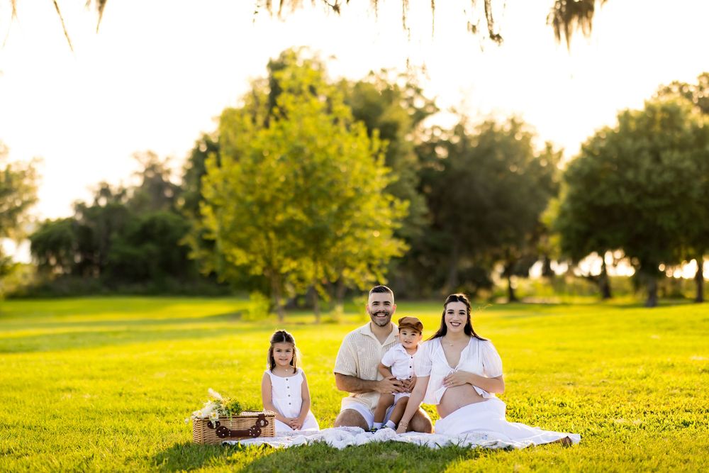 Family lounging on white blanket during sunset photoshoot in park setting. Photo by Dani De La Rosa, DigitalMyst Photography, Wesley Chapel