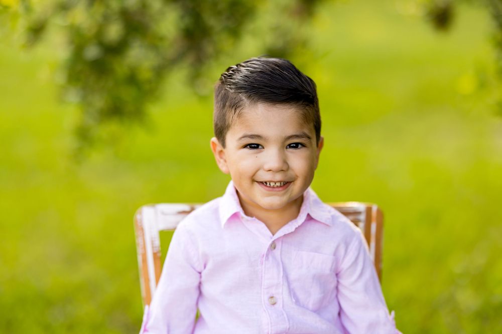 Child smiling brightly while sitting on a chair during an outdoor photo session. Photo by Dani De La Rosa, DigitalMyst Photography, Florida