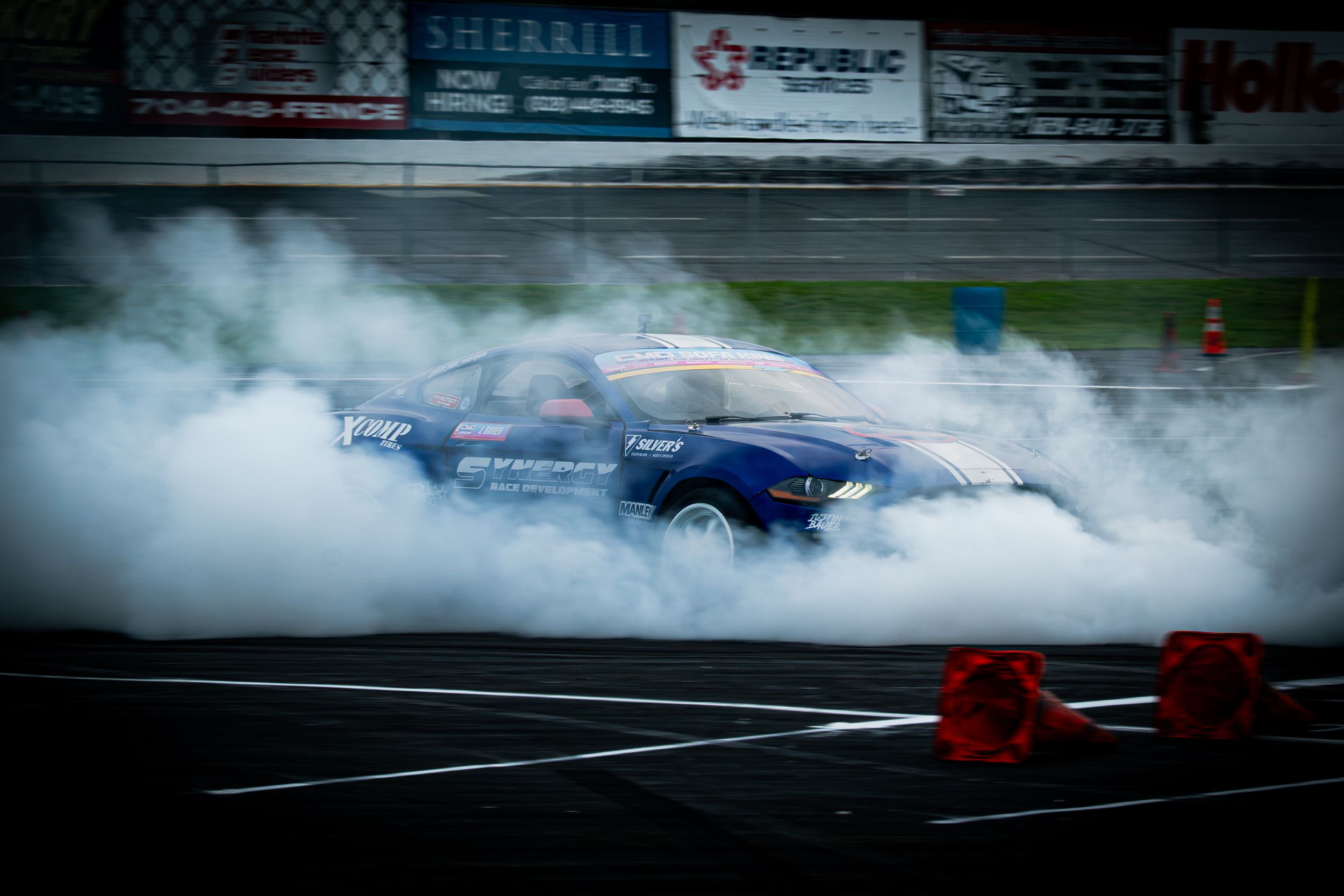 Blue drift car engulfed in tire smoke on a racing track during a high-speed drift competition.