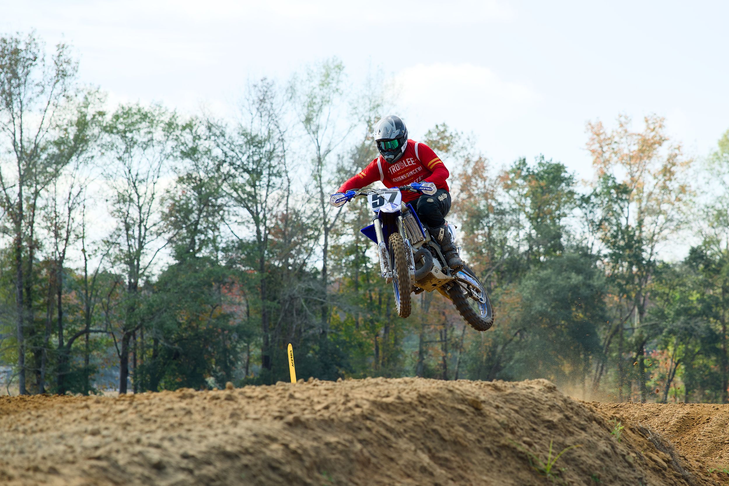 Motocross bikes performing aerial jumps on a dirt track with trees in the background.
