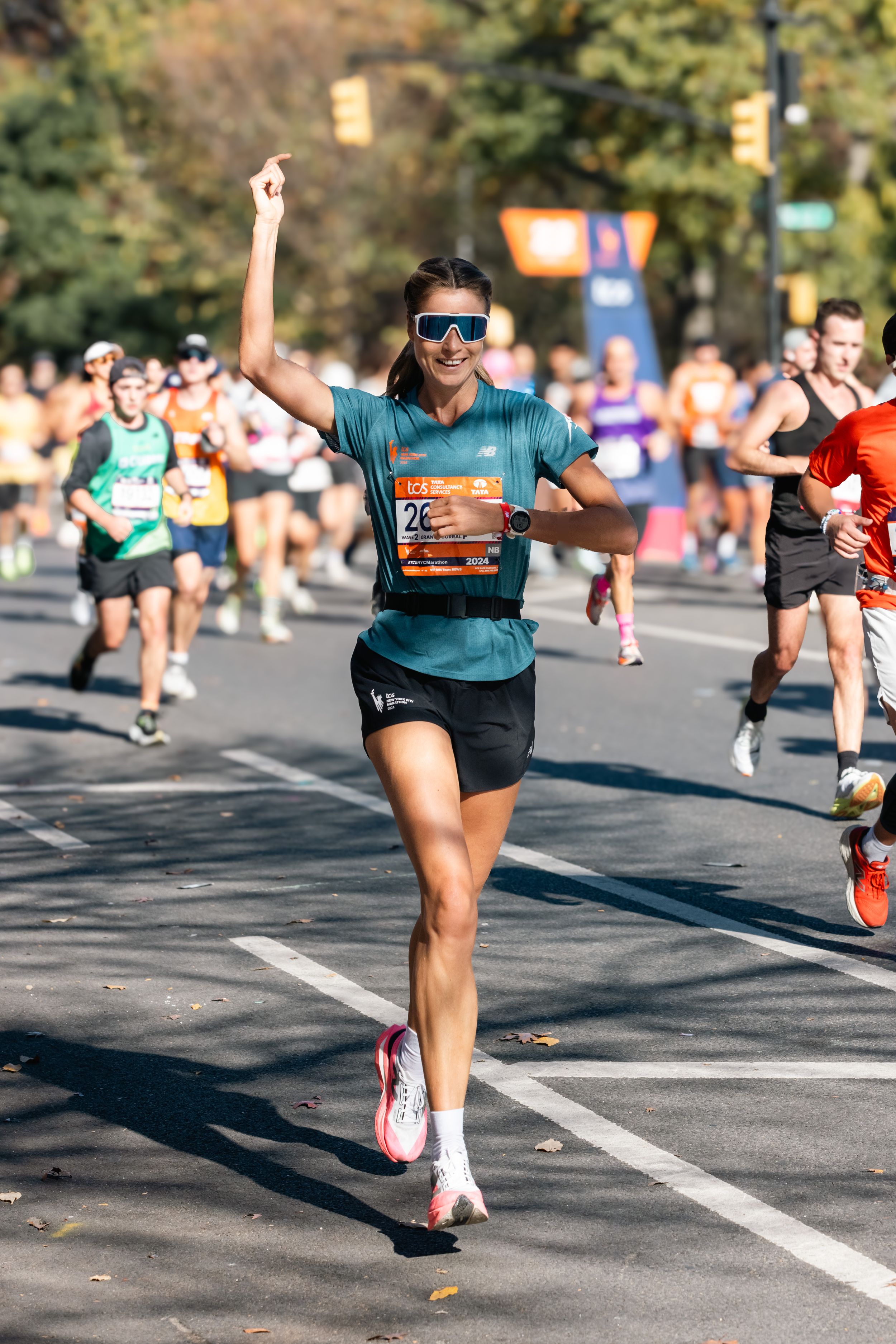 Marathon runner in teal shirt celebrates while racing through city streets.