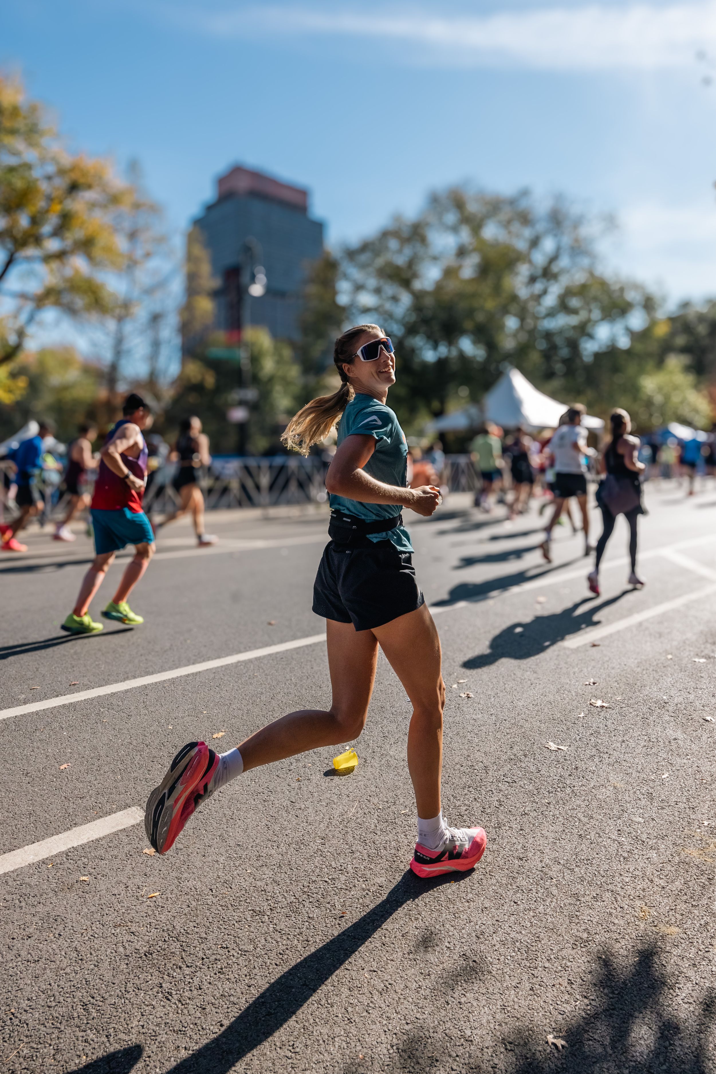Runner in teal shirt competing in marathon on sunny urban street.
