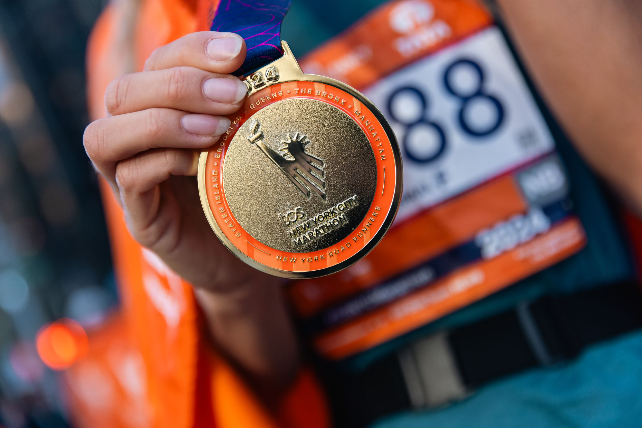 Close-up of marathon finisher medal with orange ribbon against blurred background.