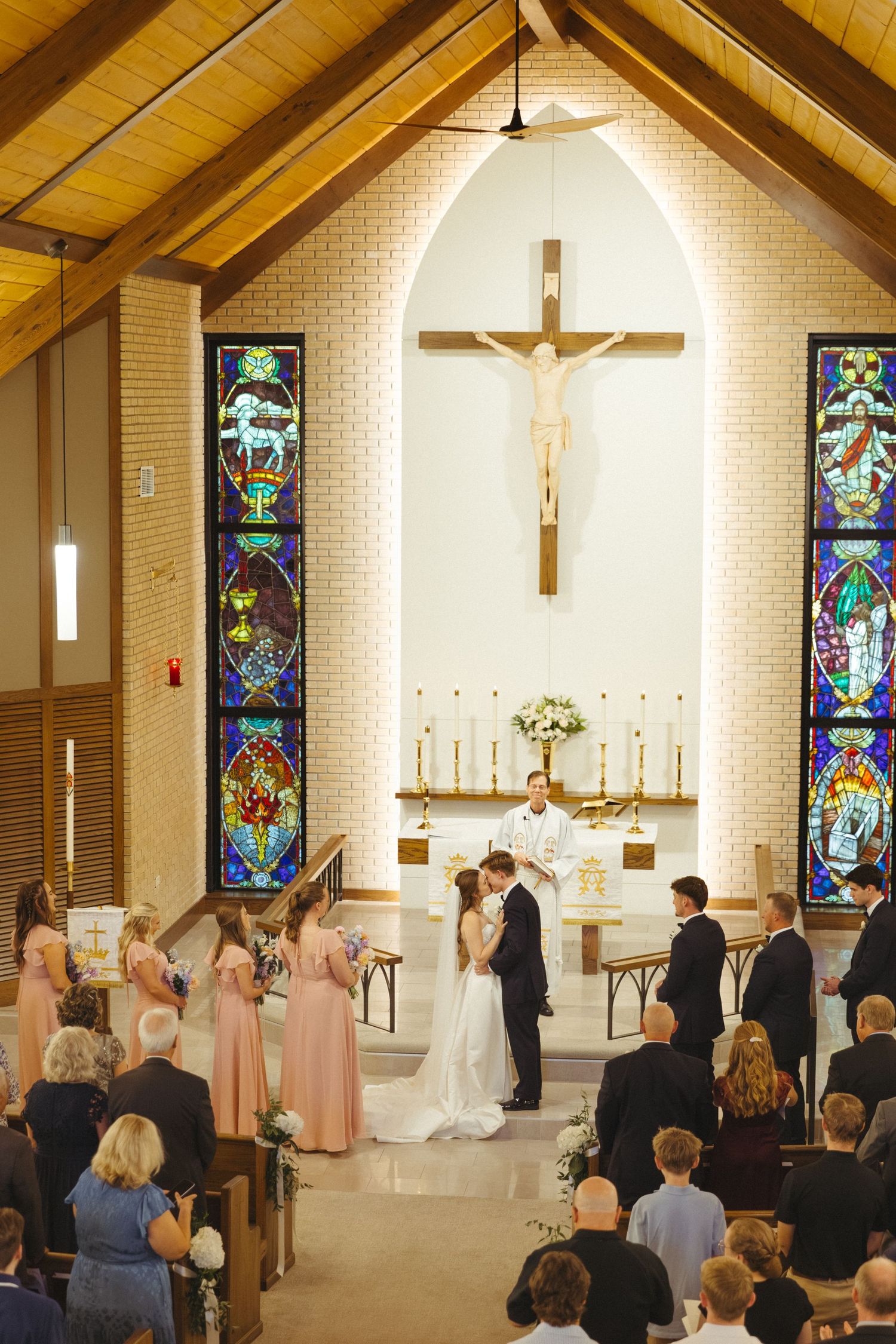 A wedding ceremony takes place in a church with beautiful stained glass windows and wooden beams.