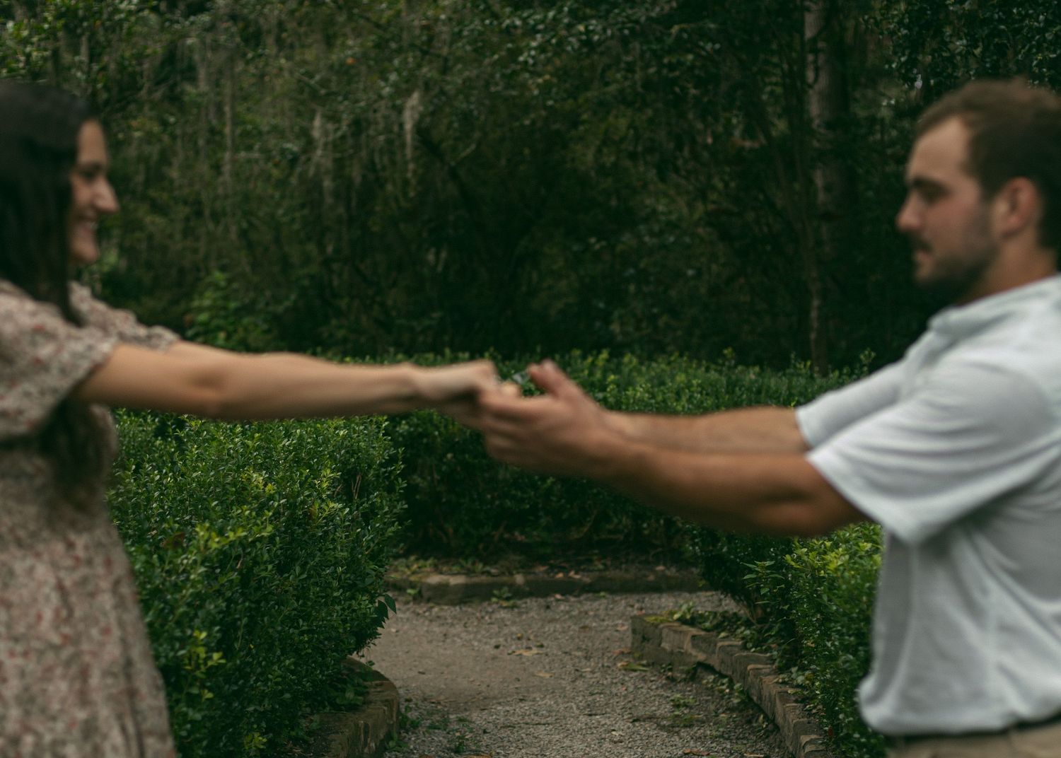 Two people playfully reaching out towards each other on a garden path.