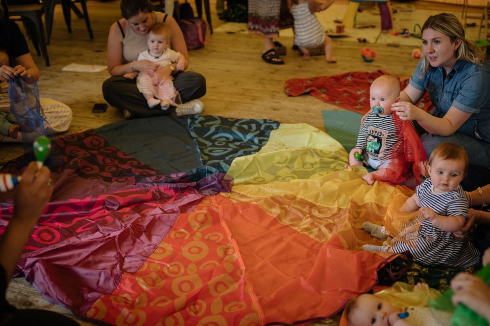 Group activity session with babies and caregivers on rainbow-colored floor mats.