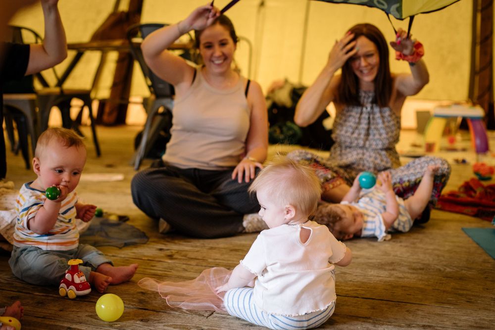 Lively group activity with babies and adults enjoying playtime on wooden floors.