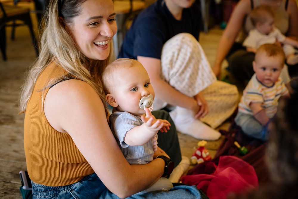 Group gathering with babies and caregivers sitting on floor during social activity.