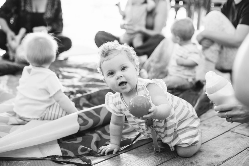 A black and white photo shows babies participating in a parent-and-child playtime session on wooden floors.
