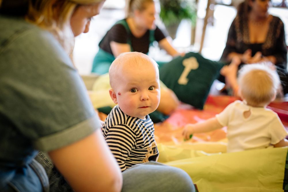 A baby in striped clothing participates in an interactive group session on colorful mats.