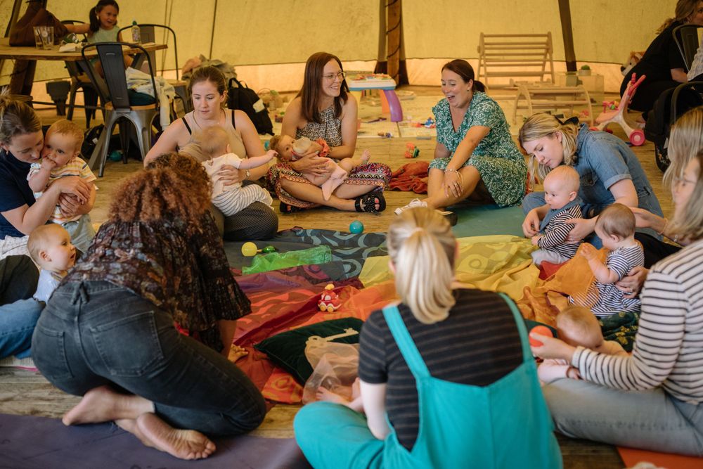 Parents and children sit in a circle on colorful mats during a group activity session.