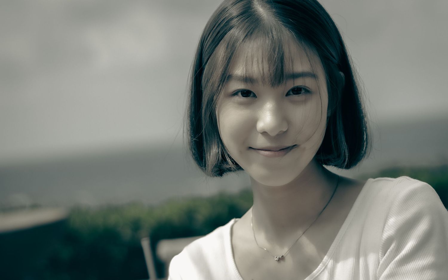 Portrait of a person in white clothing with short black hair against a blurry background.